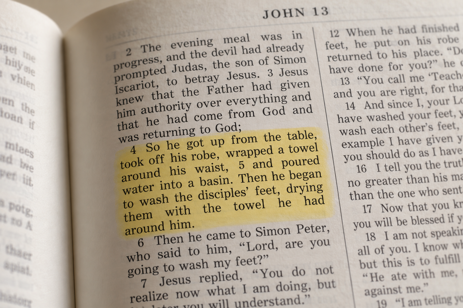 Close-up of a Bible open to John 13, highlighting verses 4-5 where Jesus gets up, wraps a towel around his waist, poured water into a basin, and begins to wash the disciples' feet.