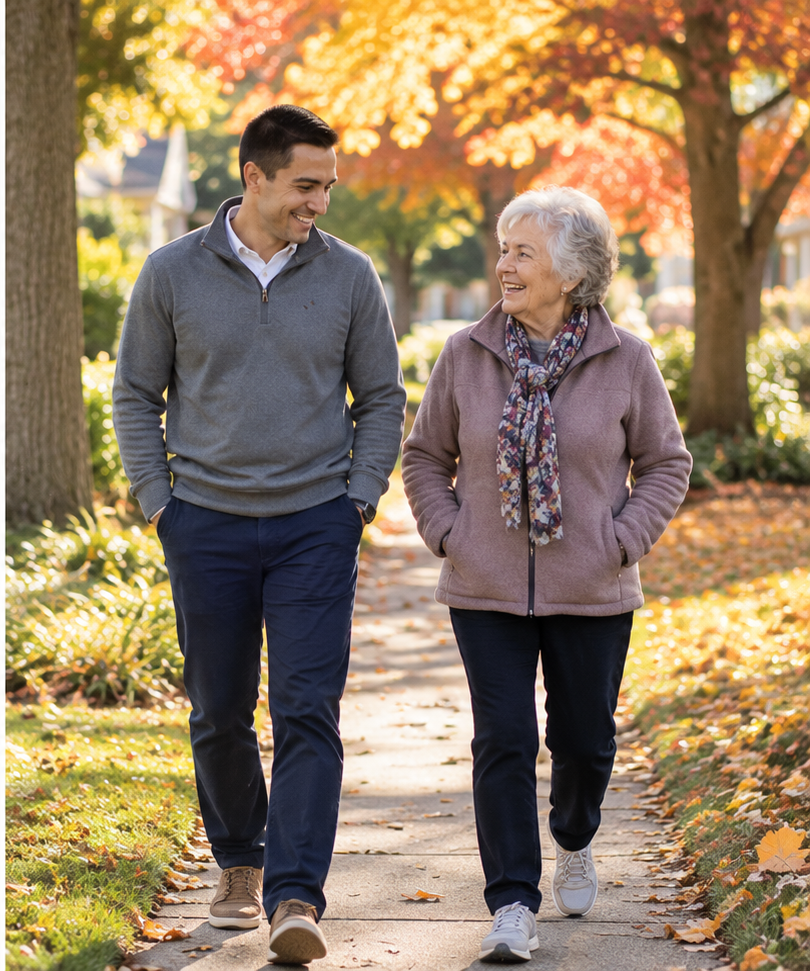 Man and elderly woman walking together on a tree-lined sidewalk in autumn