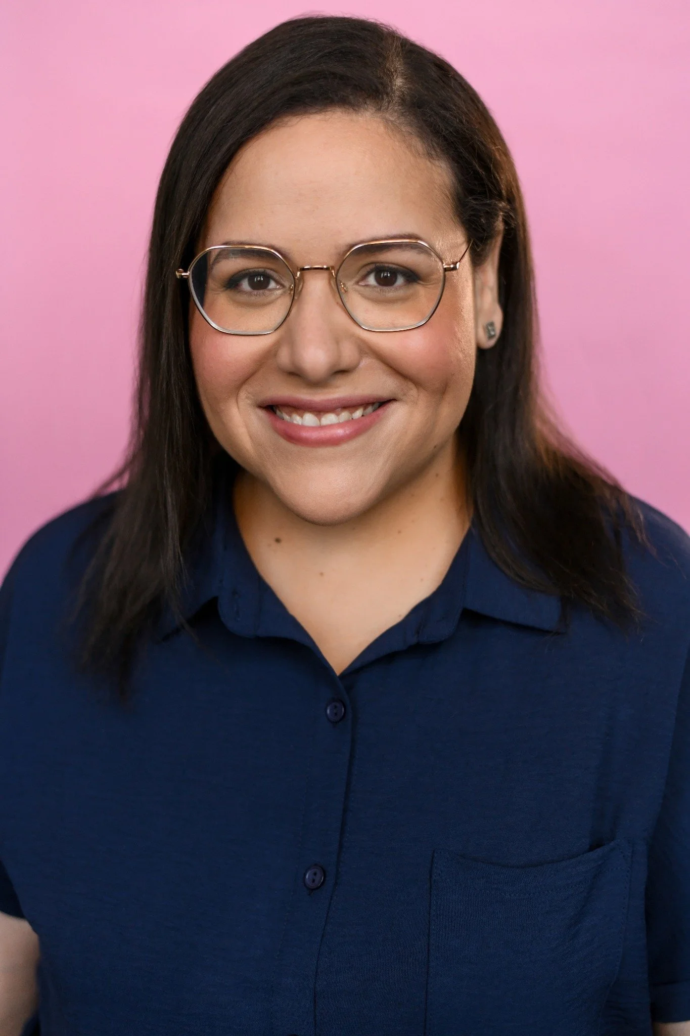 Vilmarie Rosario smiling, wearing glasses against a pink background.