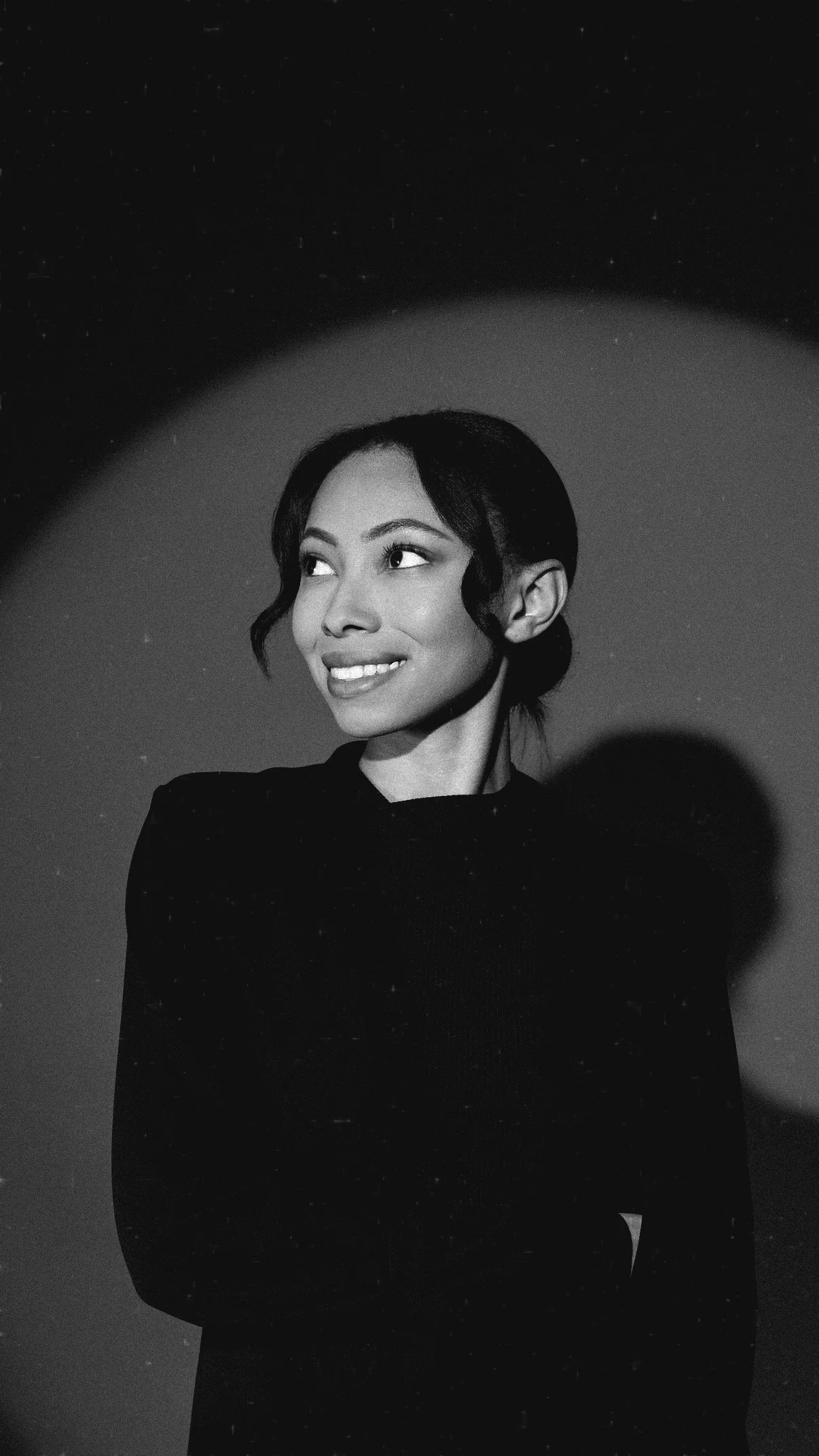 Black-and-white portrait of a Bree Stephens smiling in a black outfit looking to the side against a textured wall.