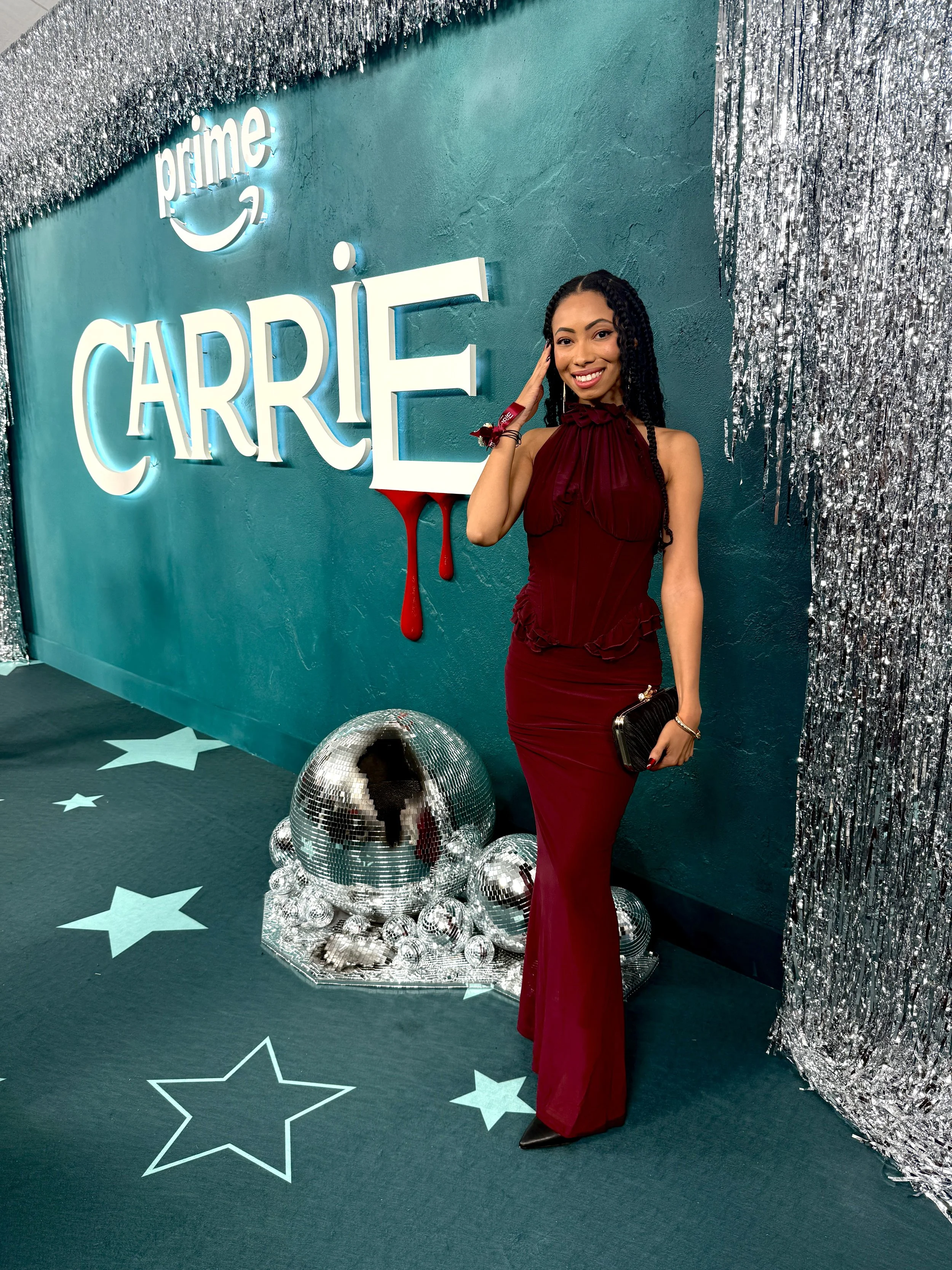 Bree Stephens in a burgundy dress posing beside a disco ball and silver tinsel at the NY Carrie Premiere