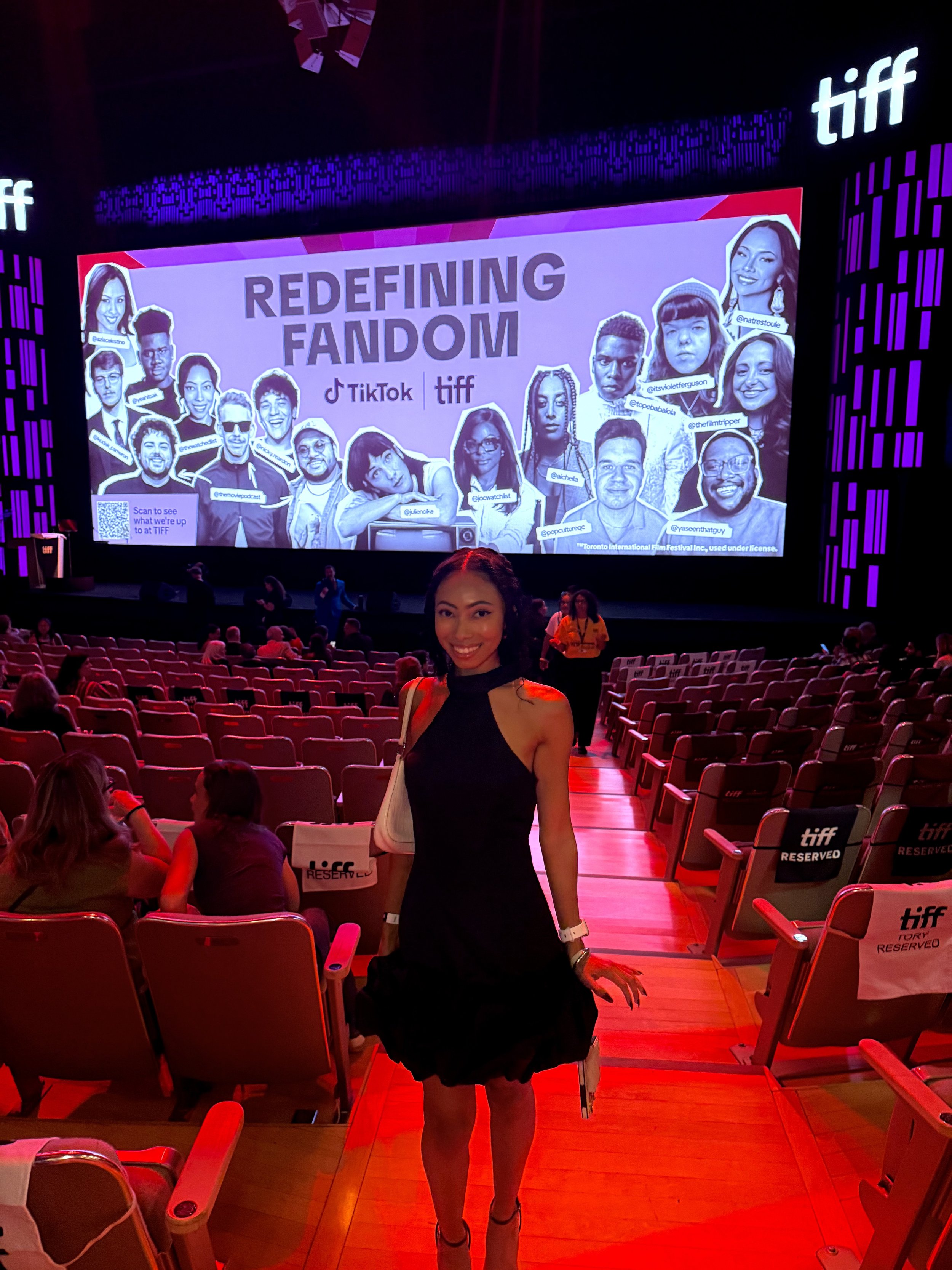 Bree Stephens posing in a movie theater beneath a TIFF TikTok presentation screen reading “Redefining Fandom,” surrounded by red reserved seats.