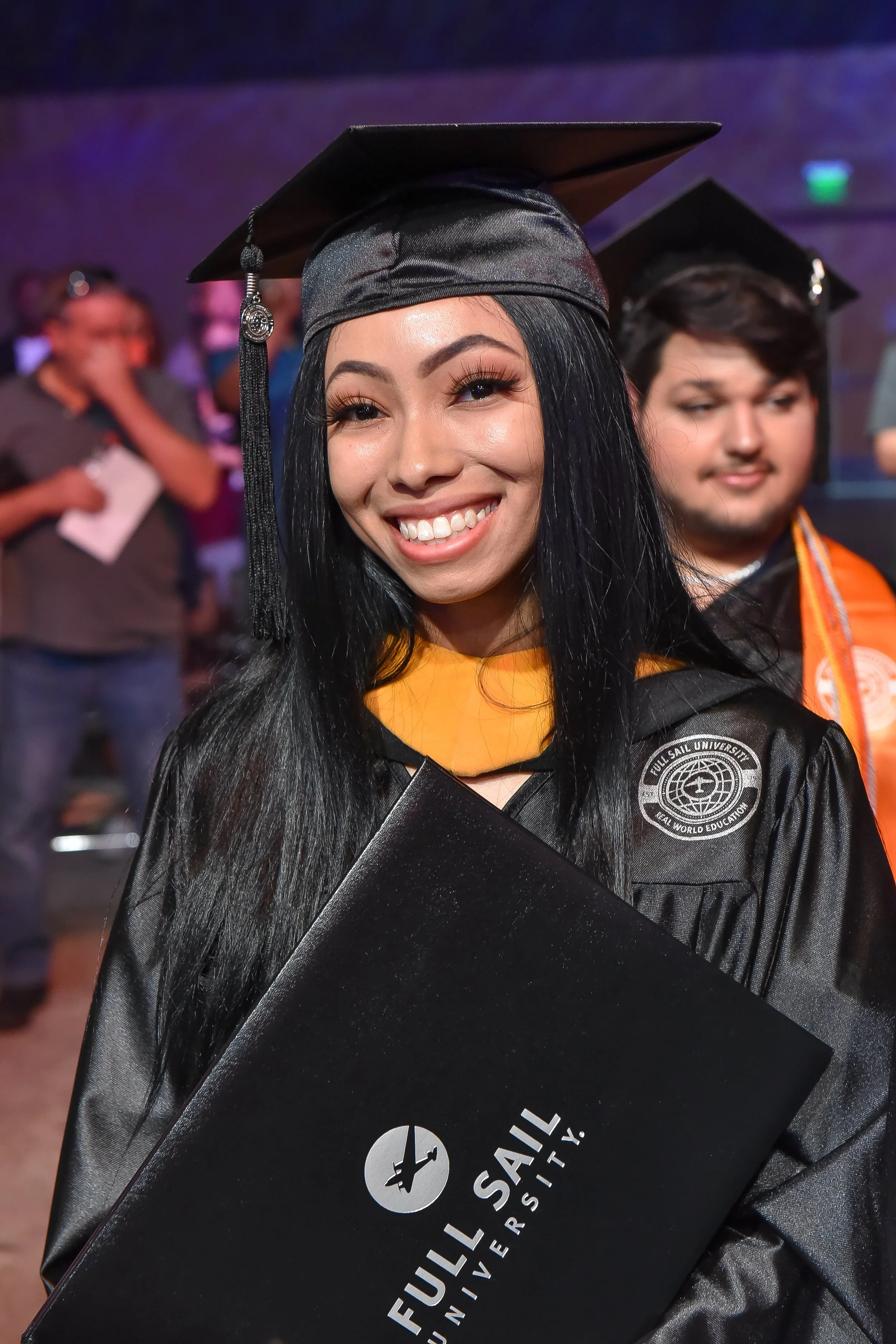 Bree Stephens smiling during graduation ceremony in black cap and gown holding a Full Sail University diploma.