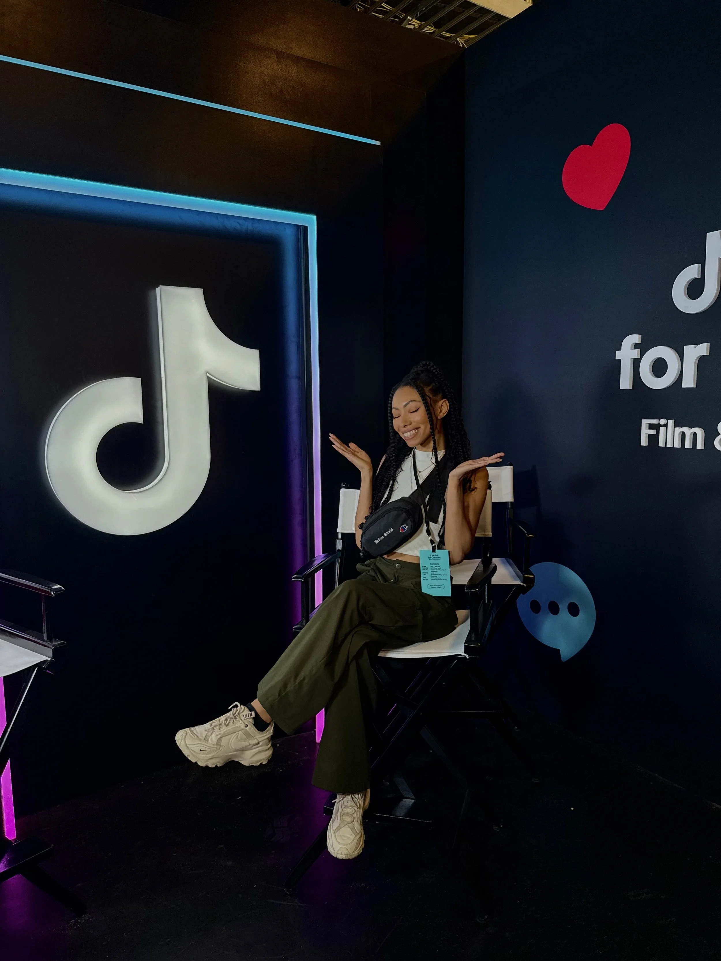 Bree Stephens seated in a director’s chair at a TikTok Film & TV event booth with neon lighting.