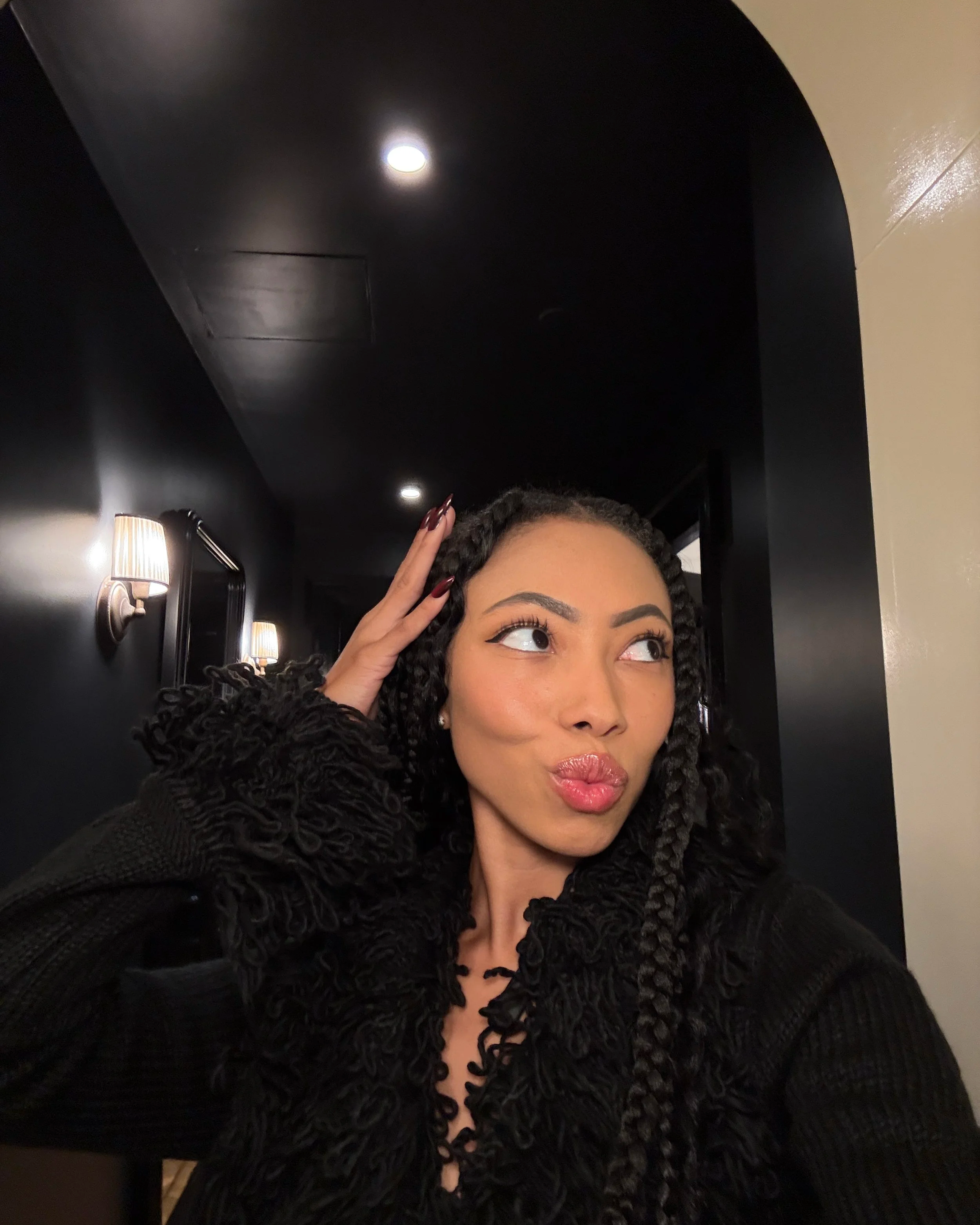 Bree Stephens with curly box braid making a playful kissy face in a dimly lit New York Hotel room
