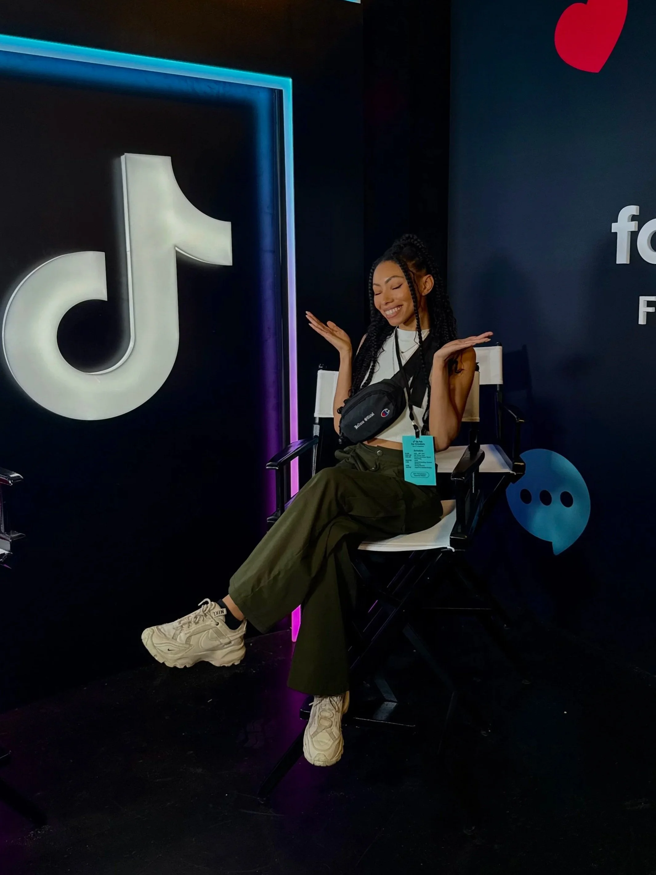 Bree Stephens with long braids sitting in a director’s chair at a TikTok-themed event, wearing a crossbody bag and green pants.