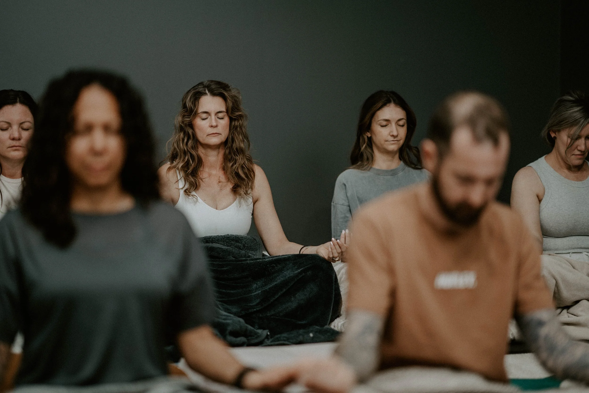 People meditating with closed eyes, seated on the floor in a calm setting.