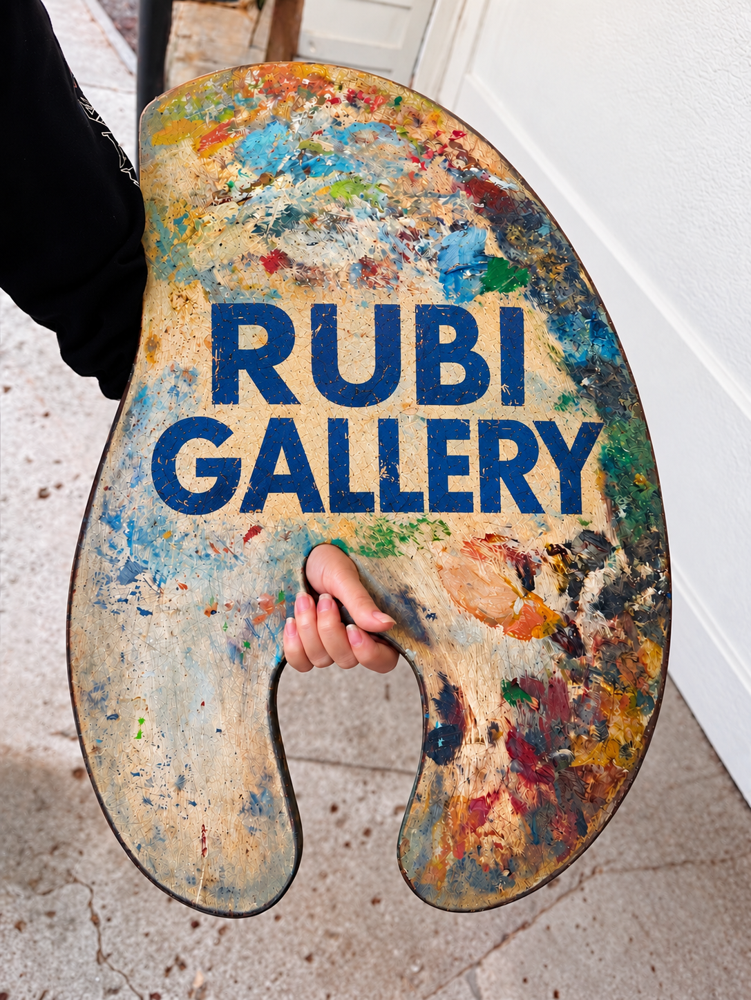 Artist's arm holding a painter's palette with the words Rubi Gallery, an independent mobile art gallery based in Santa Barbara, California