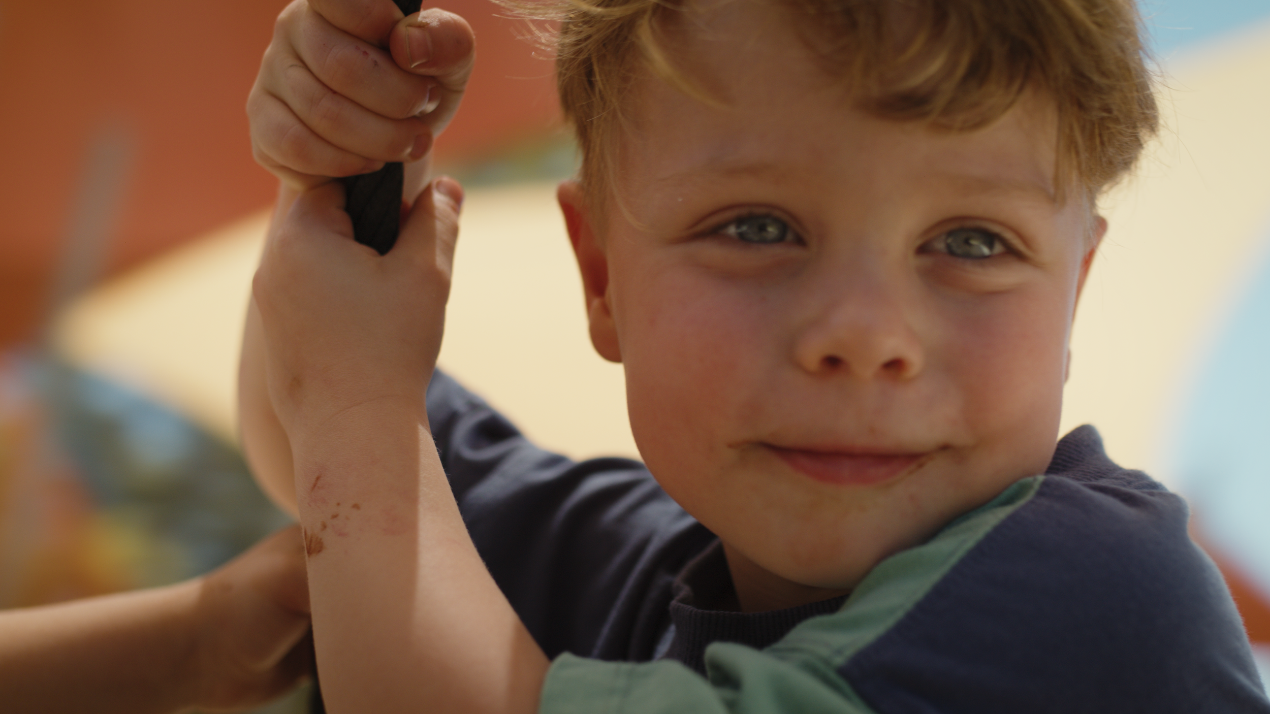 A young boy smiles at the camera as he holds the chain of a swing.