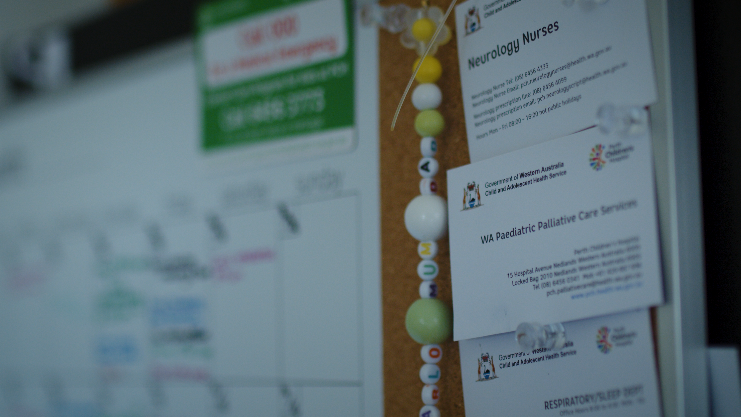 A noticeboard with medical contact cards and a string of colourful beads.