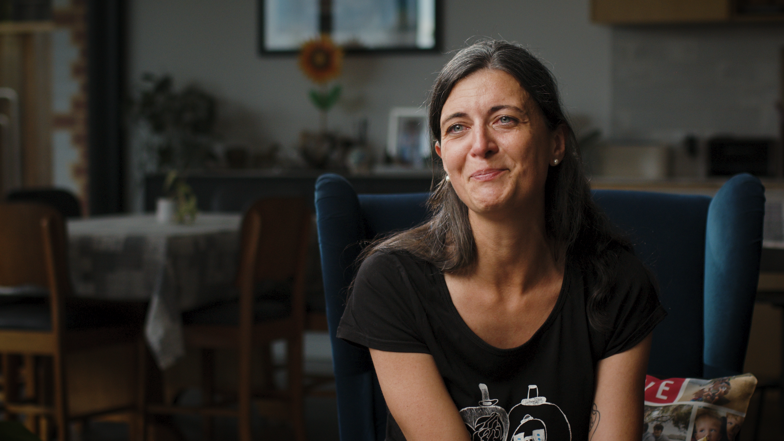 A parent carer sits in a blue armchair at home, smiling during her interview.