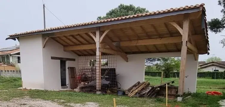 Abri de jardin en bois et tuiles avec outils et matériaux de construction dans une cour rurale.