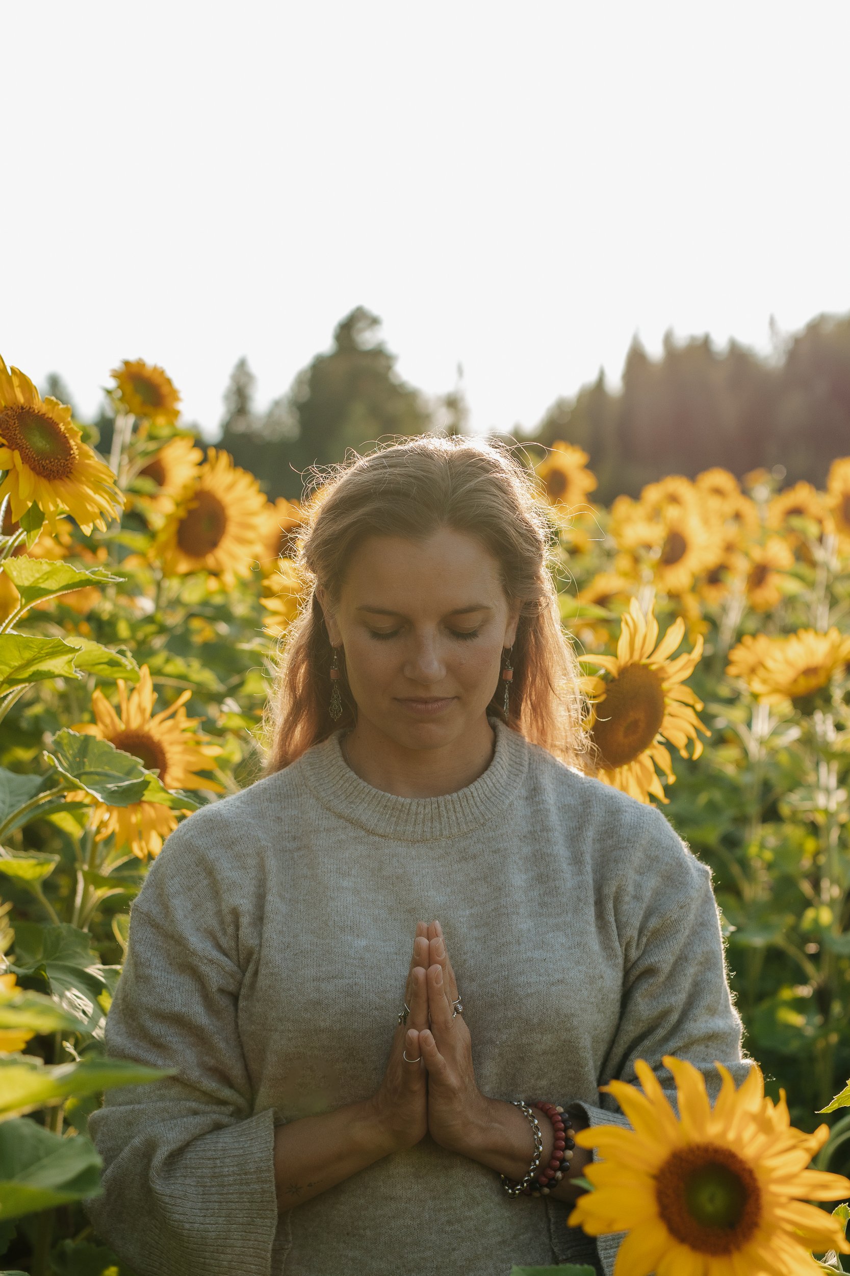 Nainen meditoi kädet rukousasennossa auringonkukkapellolla.