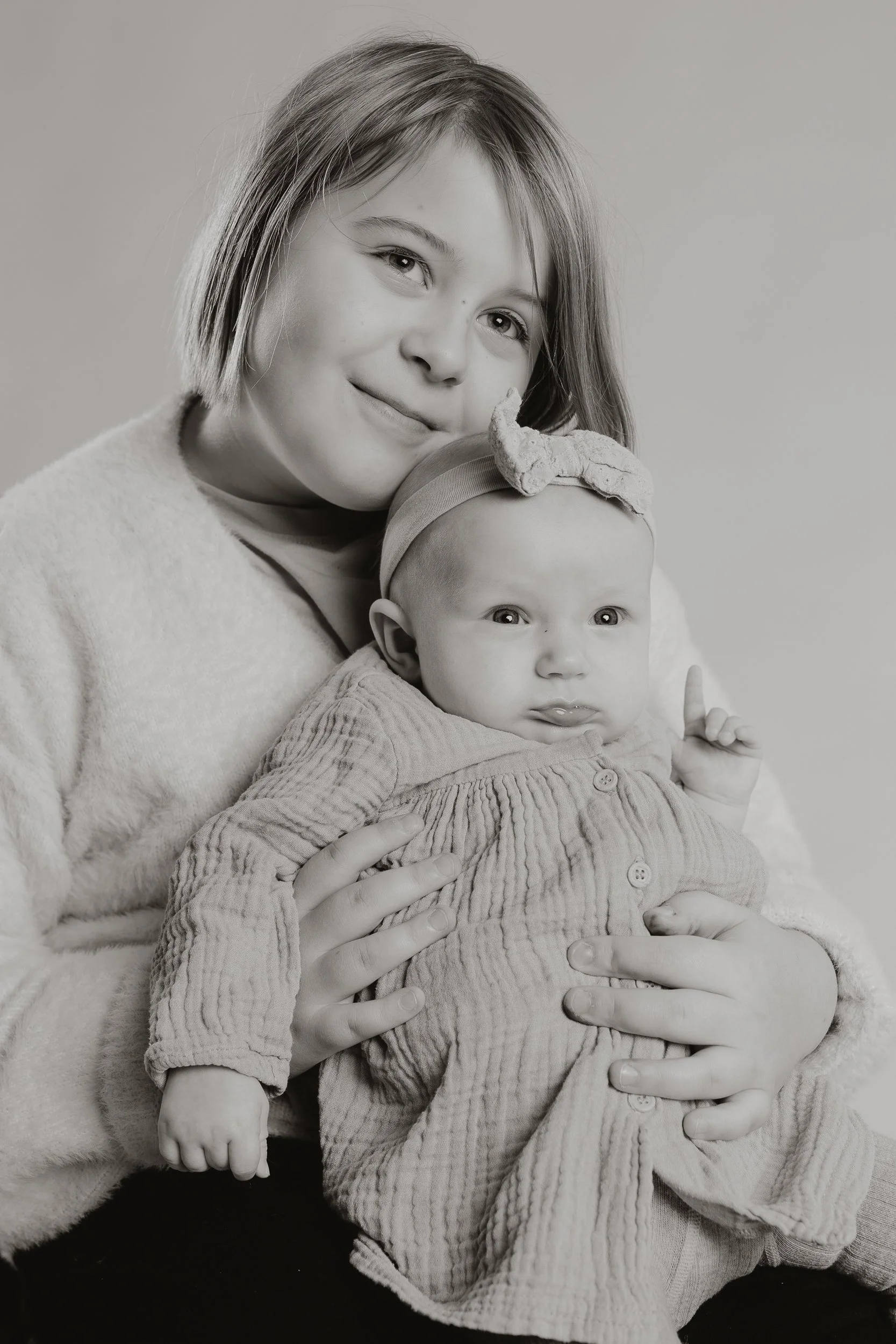 Mustavalkoinen muotokuva äidistä pitelemässä vauvaa, jolla on rusetillinen hiuspanta.
