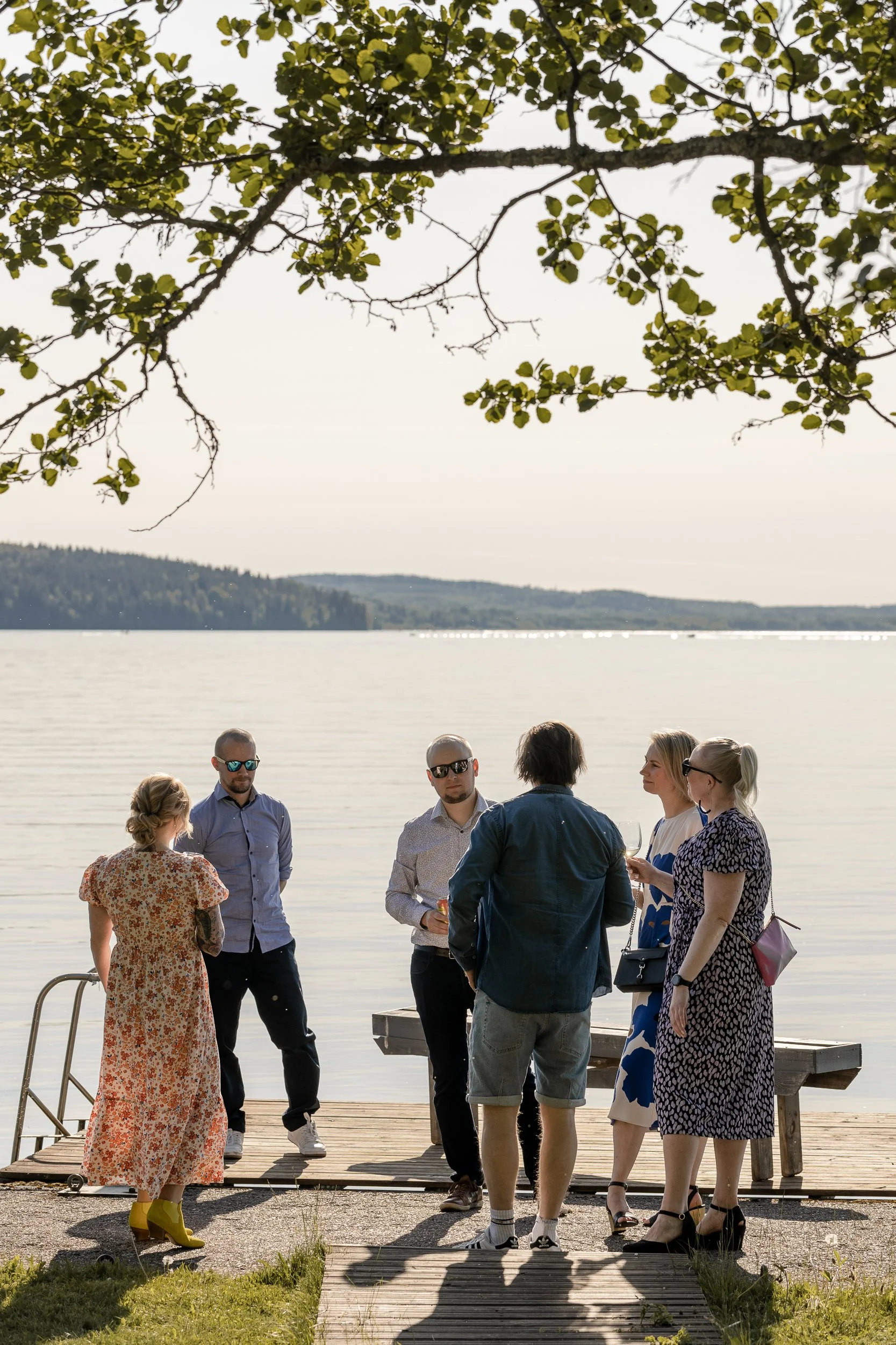 Ryhmä ihmisiä keskustelemassa järven rannalla laiturilla aurinkoisena kesäpäivänä