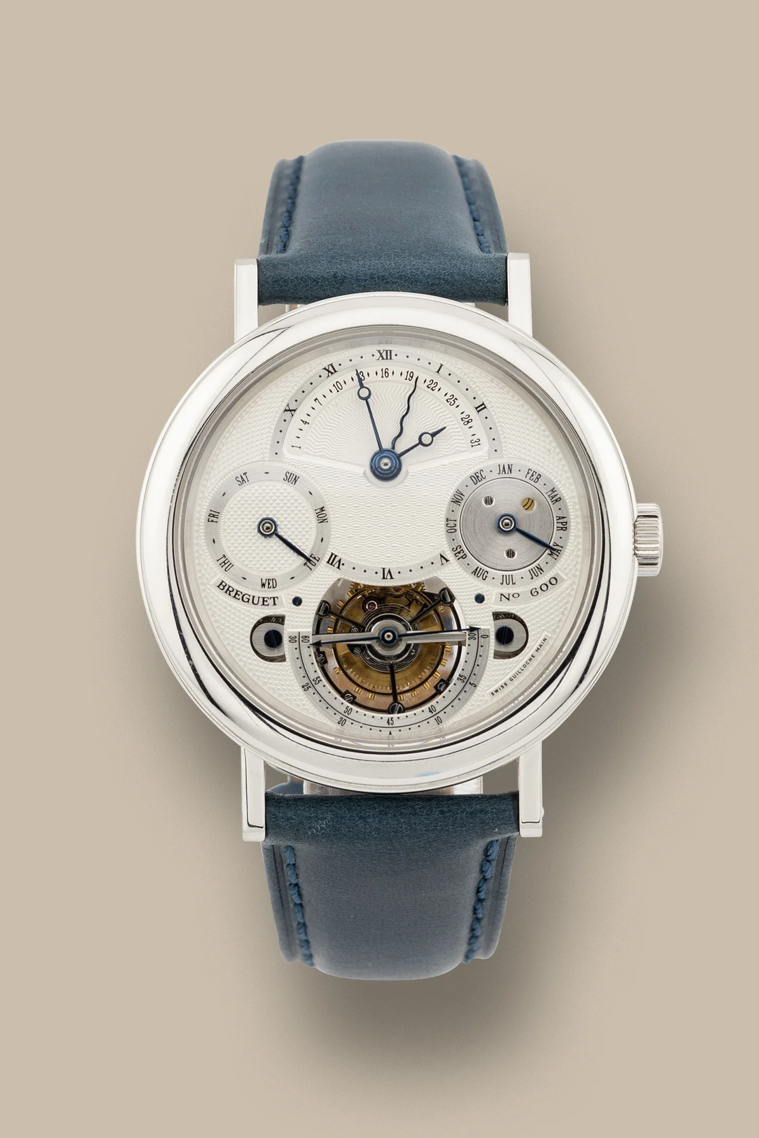 Close-up of a luxury wristwatch with a silver case and a white face, featuring multiple dials and a visible mechanical movement, with a dark blue leather strap.