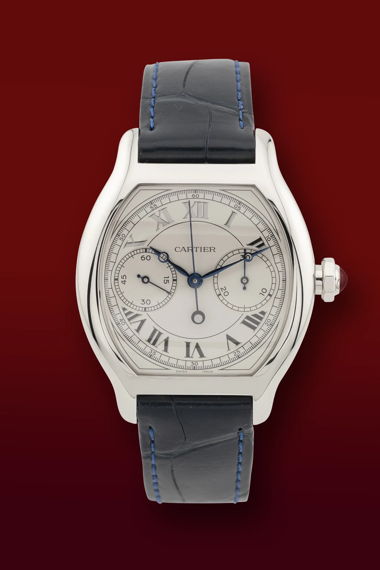 Close-up of a Cartier wristwatch with a white dial, Roman numerals, and a black leather strap with blue stitching, set against a red background.