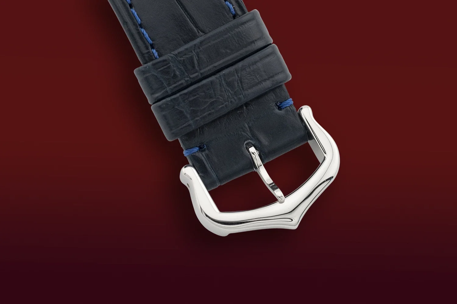 Close-up of a black leather watch strap with a shiny silver buckle on a red background.