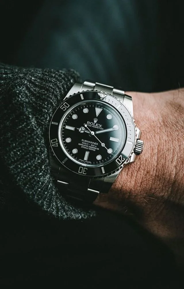 Close-up of a Rolex Submariner watch on a person's wrist, with a black dial and silver bracelet.