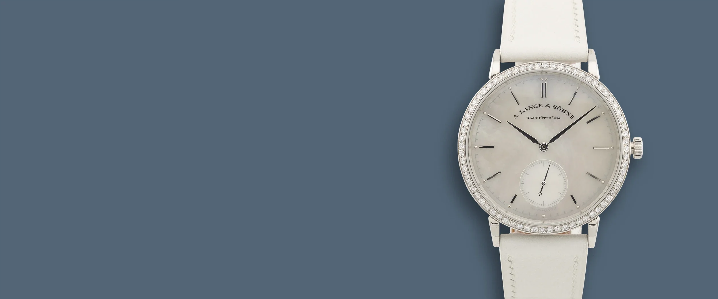 Close-up of a luxury wristwatch with a round face, diamond-studded bezel, white strap, and black hands, displaying the time.