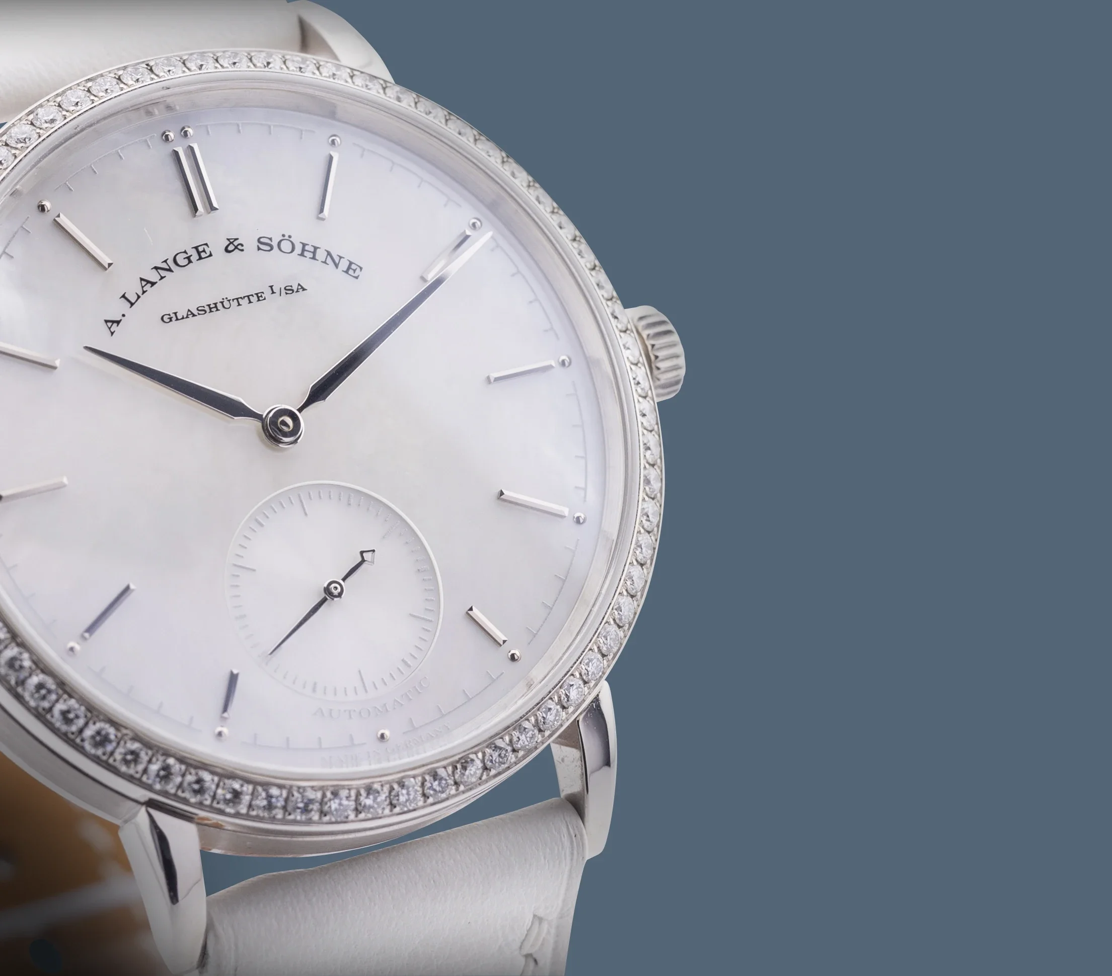 Close-up of a luxury wristwatch with a silver face, diamond-studded bezel, and black hour and minute hands, displaying the brand 'A. Lange & Söhne' and 'Glashütte I/SA' on the dial.