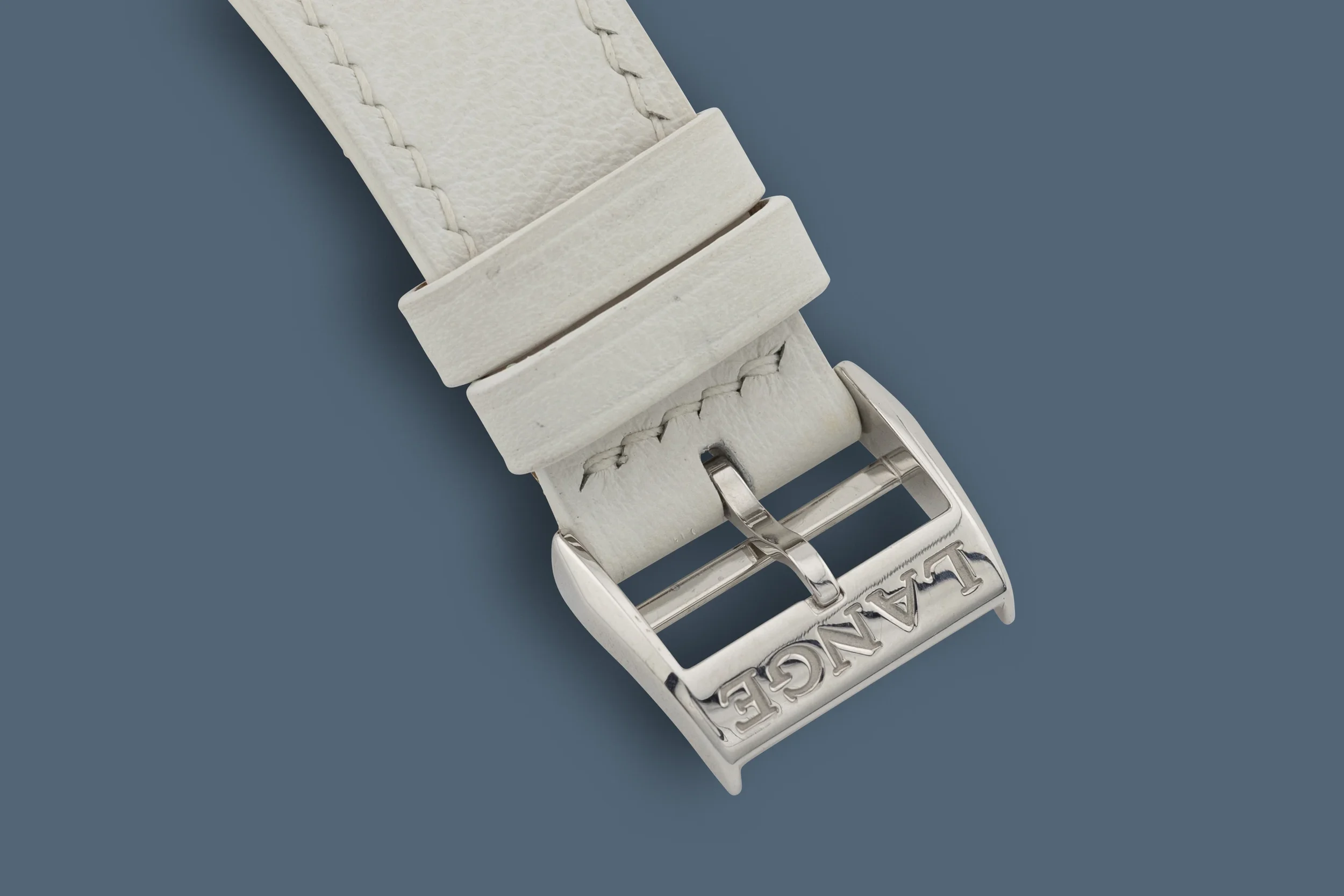 Close-up of a white leather watch strap with metal logo buckle, laying on a blue background