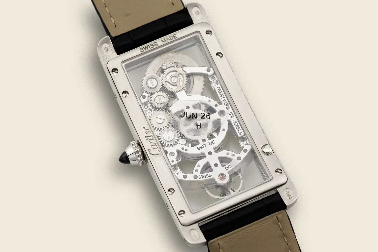 A rectangular luxury wristwatch with an exposed mechanical movement and gears, labeled 'Cartier' on the side, with a black leather strap and a beige strap. The watch face is transparent, revealing the intricate internal gears and components.