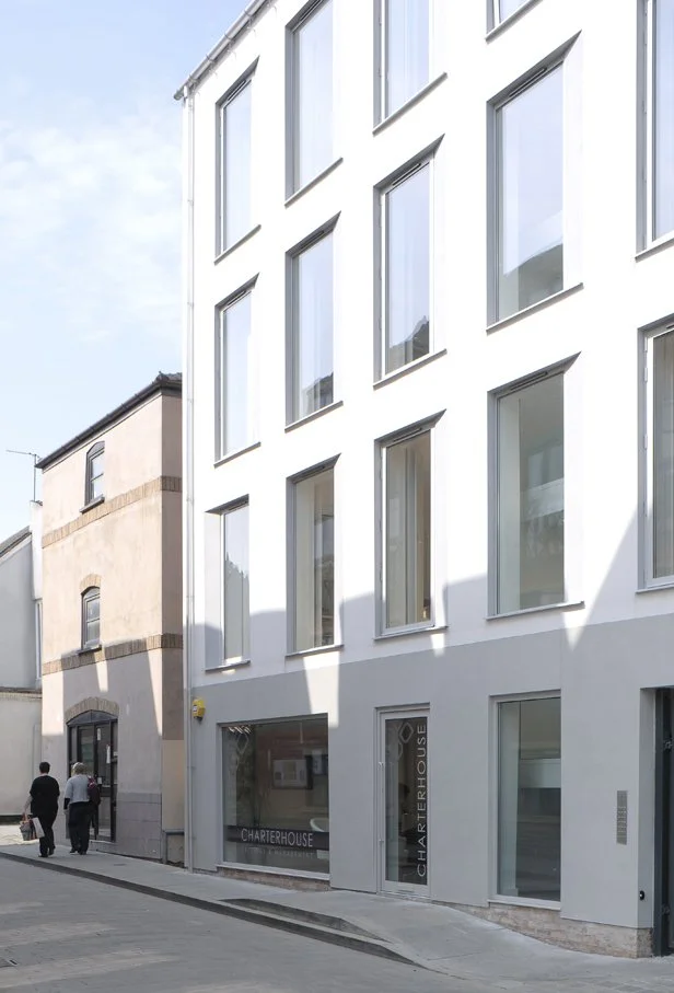 Modern white multi-story building with large windows and Charterhouse storefront on a quiet urban street
