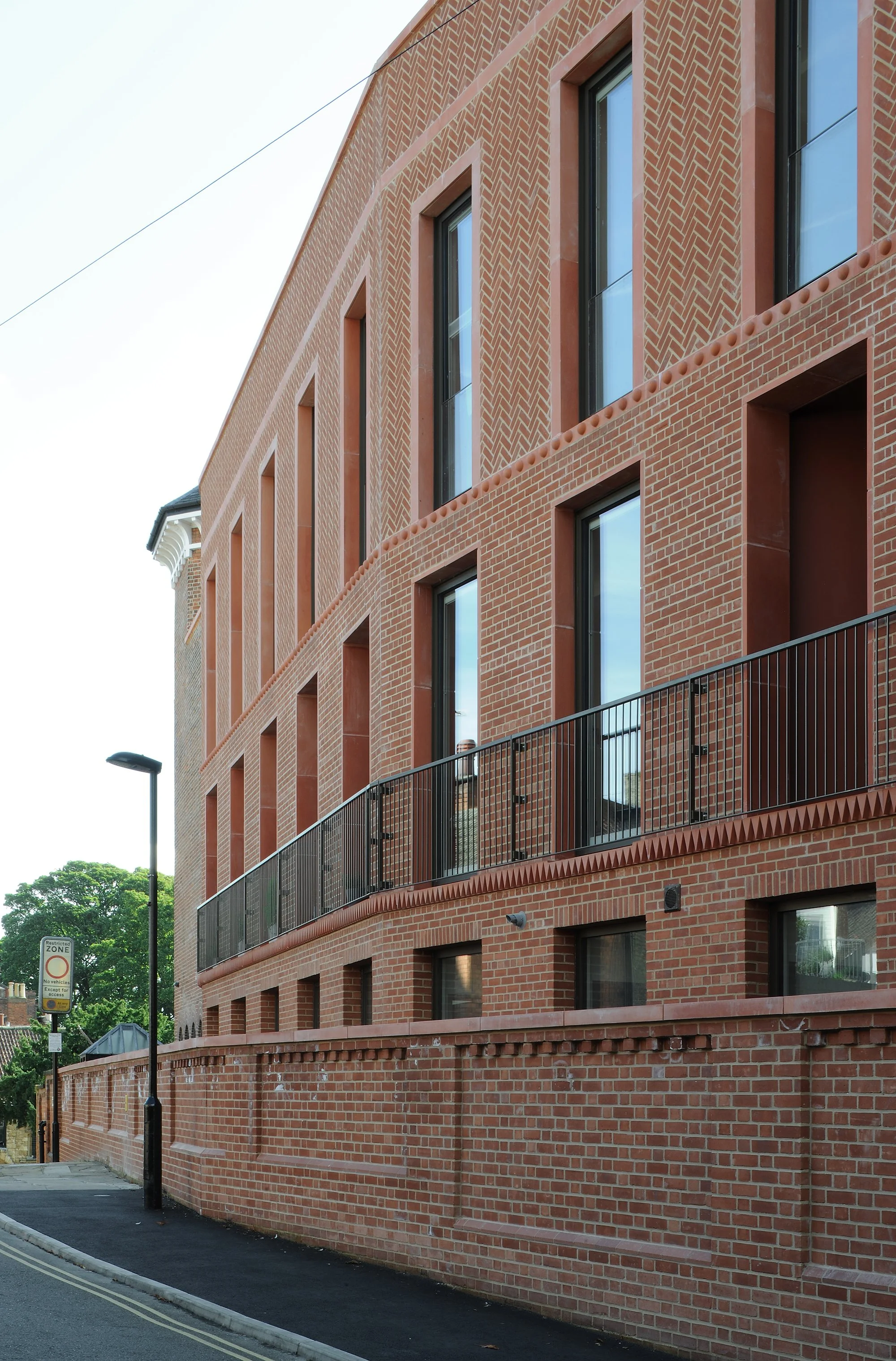 Red brick building with tall windows, balconies, decorative brickwork, and a restricted-zone street sign