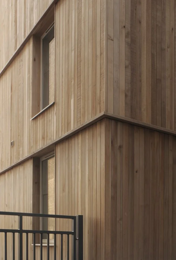 Close-up of a modern building facade with vertical wood siding, windows, and black metal railing