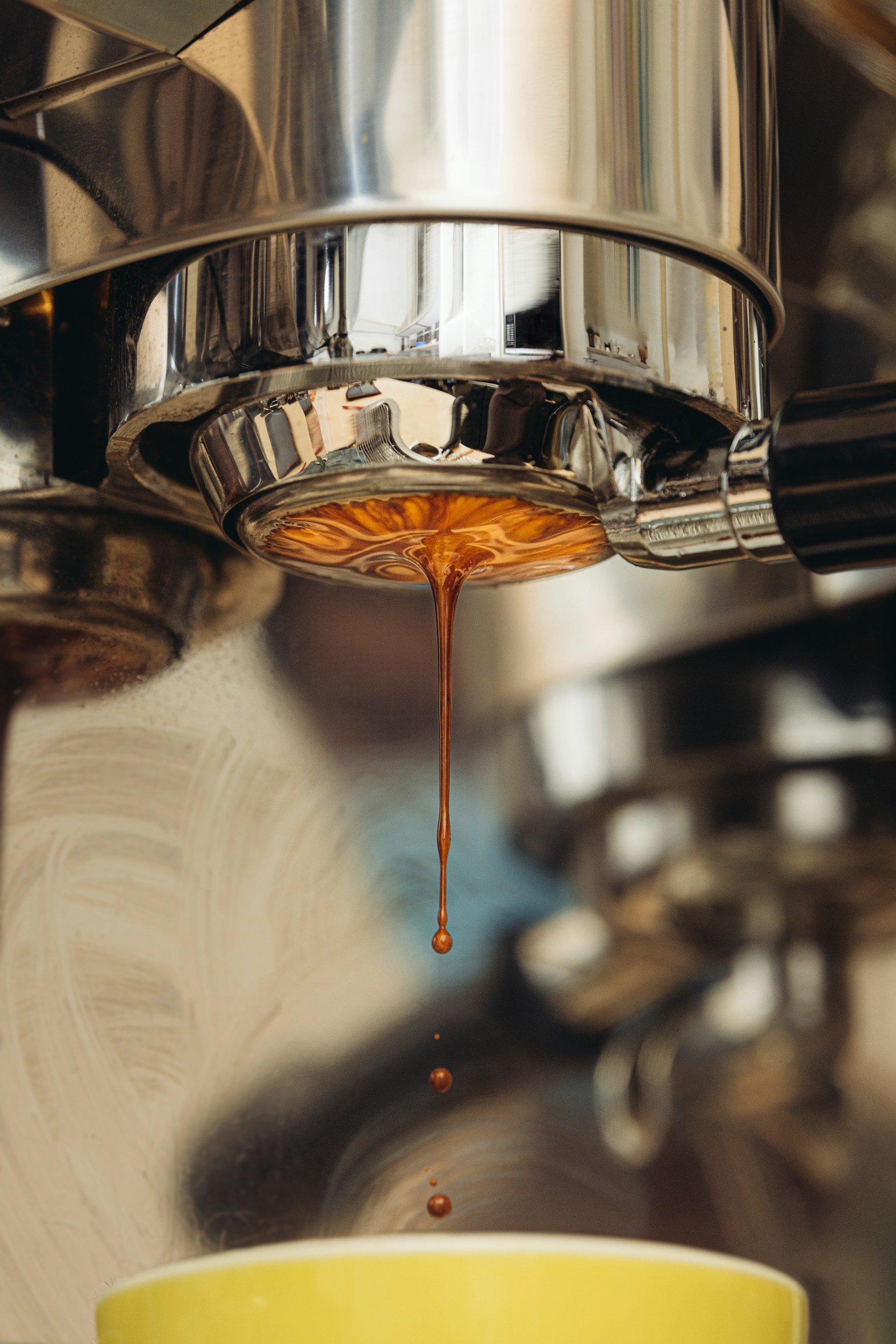 Close-up of a coffee machine dispensing dark coffee into a yellow mug.