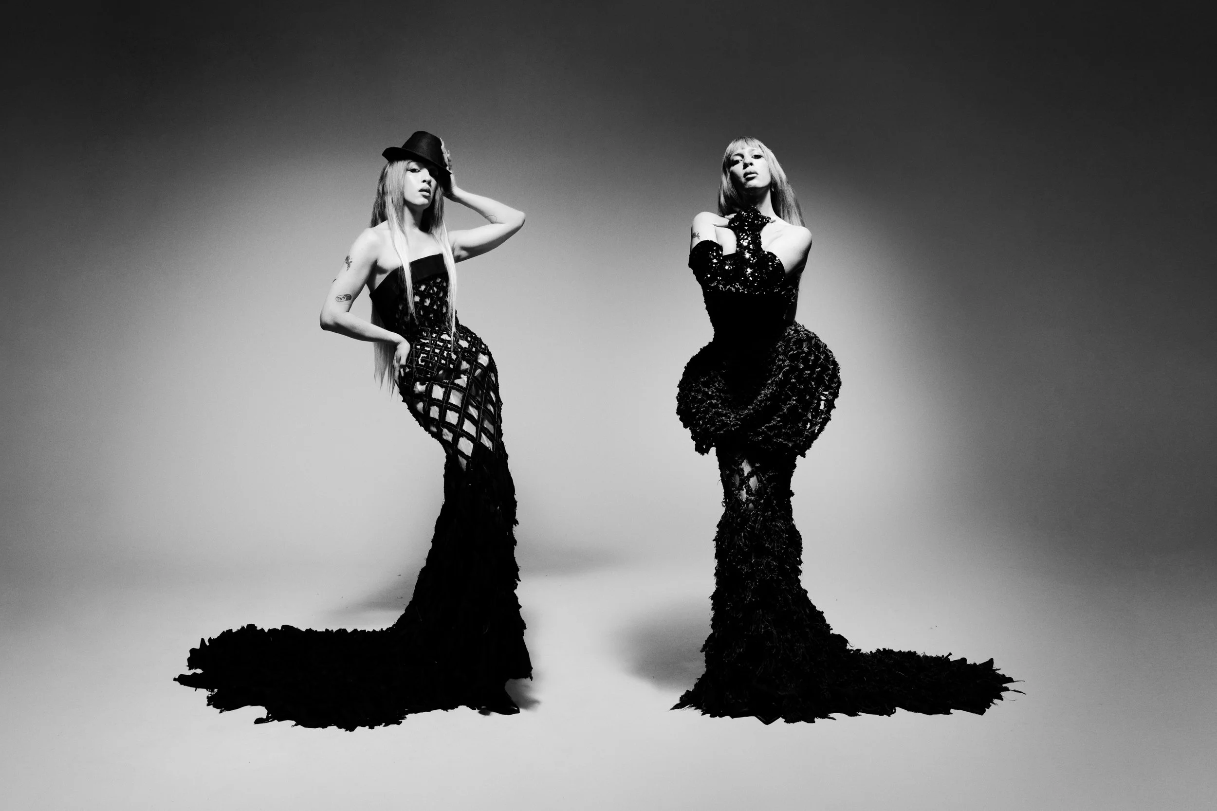 Two women in black lace dresses standing on a rocky landscape in black and white.