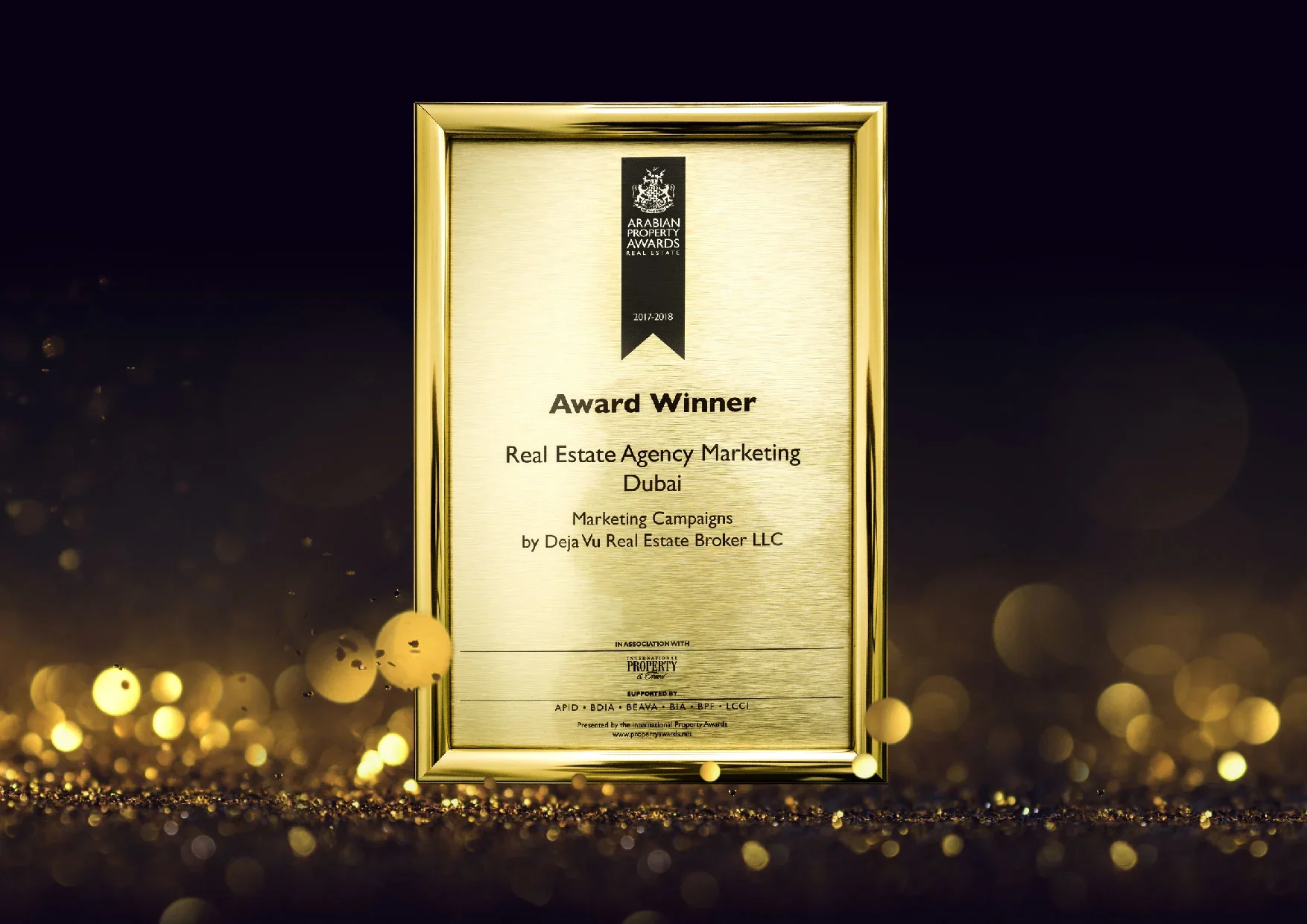 A framed award plaque with a gold border, recognizing a real estate marketing campaign for Dubai by Deja Vu Real Estate Broker LLC, presented at the Arabian Property Awards 2017-2018, with a dark background and gold bokeh lights.