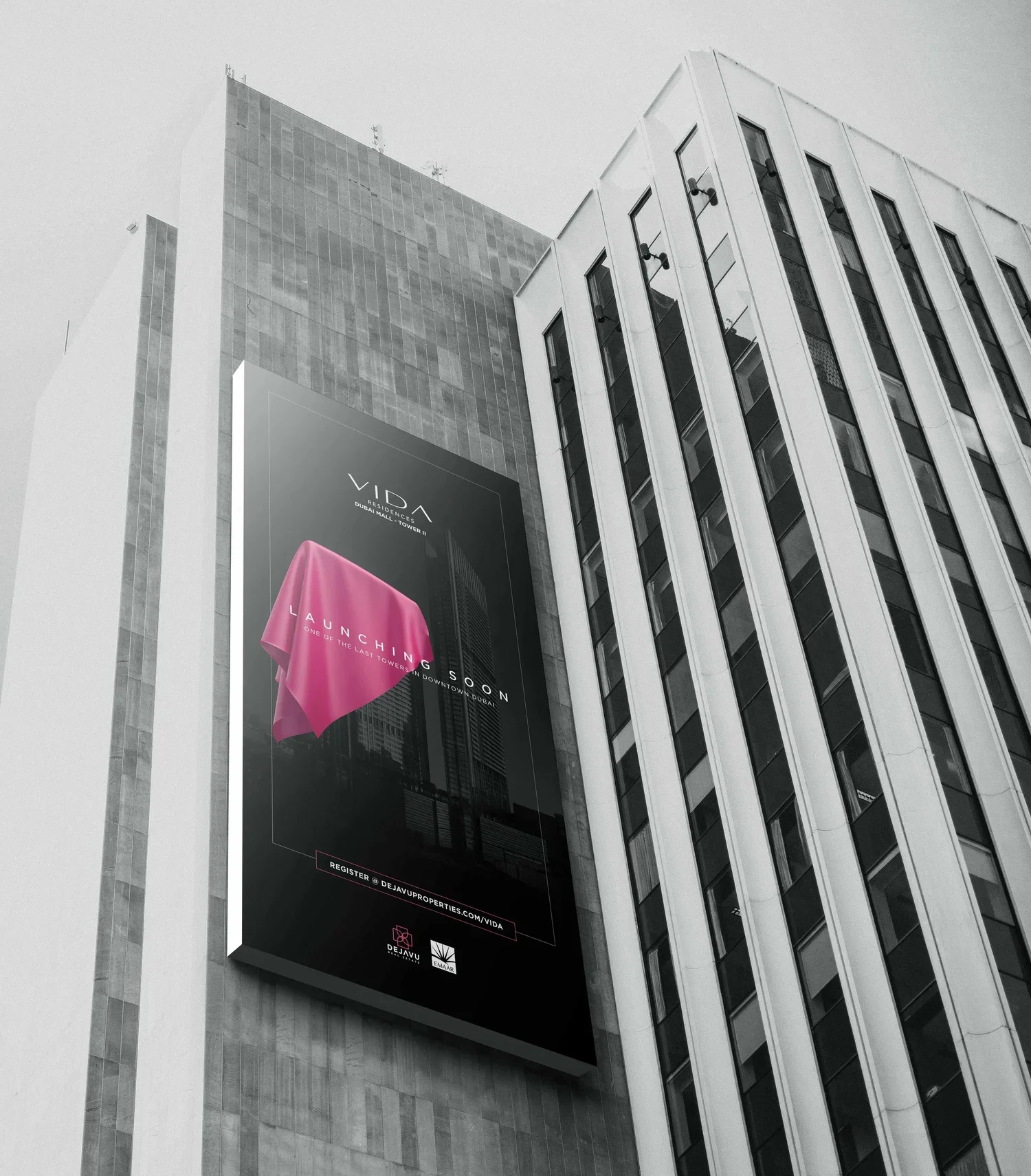 A tall modern building with a billboard advertising Vida Residences Dubai Mall Tower 2. The billboard has a pink cloth design, and the building features many windows and a gray facade.