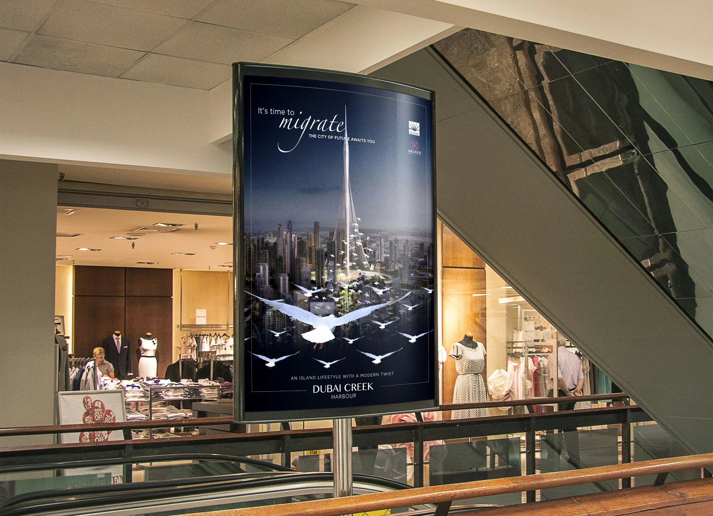 A shopping mall or retail store interior with mannequins displaying clothing and racks of clothes. A large advertisement for Dubai Creek Harbour features a modern city skyline and a tall tower with an island lifestyle theme. The ceiling has a stepped design, and an escalator is visible in the foreground.