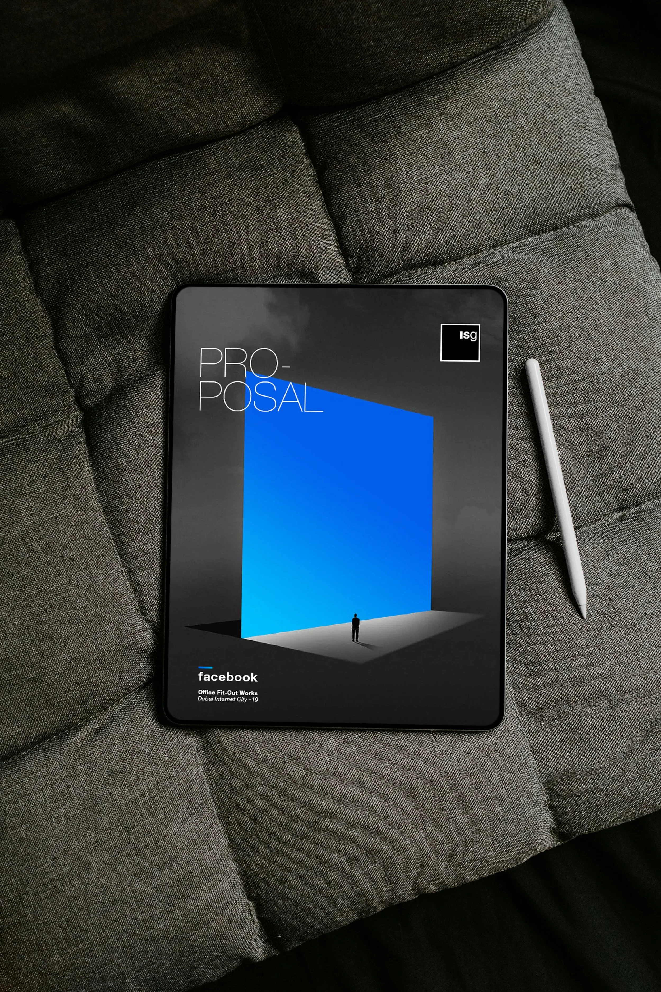 A tablet displaying the Facebook logo and branding, resting on a gray fabric couch, with a stylus pen beside it.