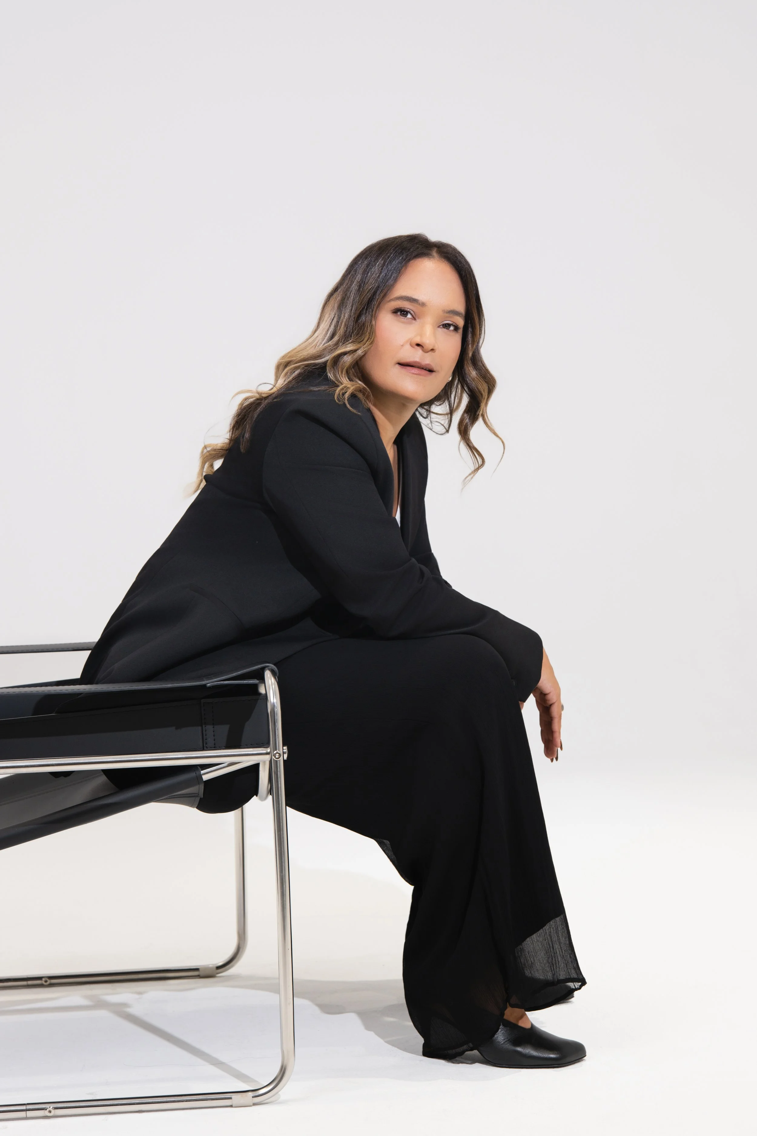 Dr. Karin Lorez, Founder of Lorez Advisory, seated on a modern chair wearing a black blazer and long black skirt against a white background.