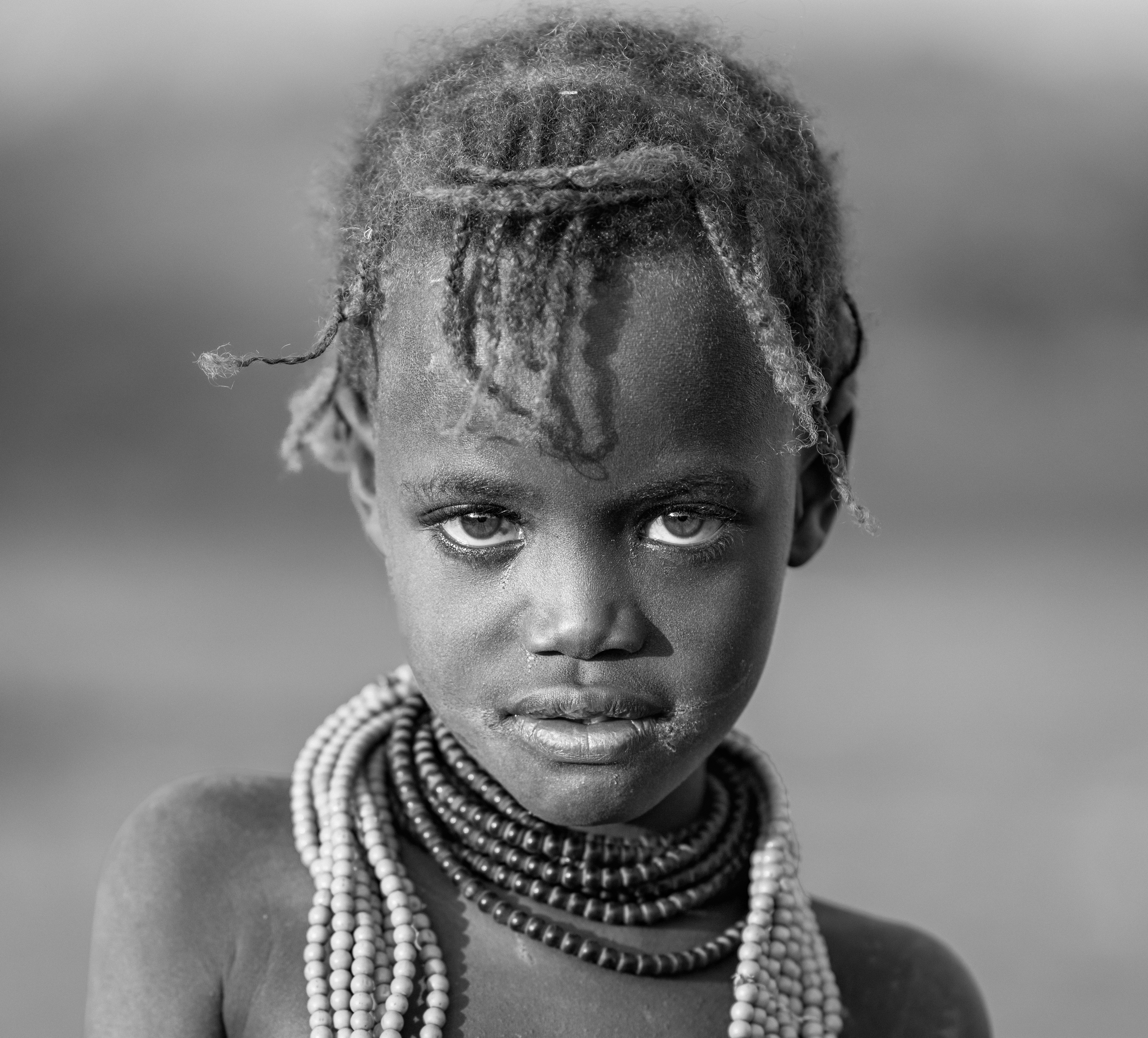 Close-up of an African woman with natural hair wearing layered pearl necklaces, looking directly at the camera.
