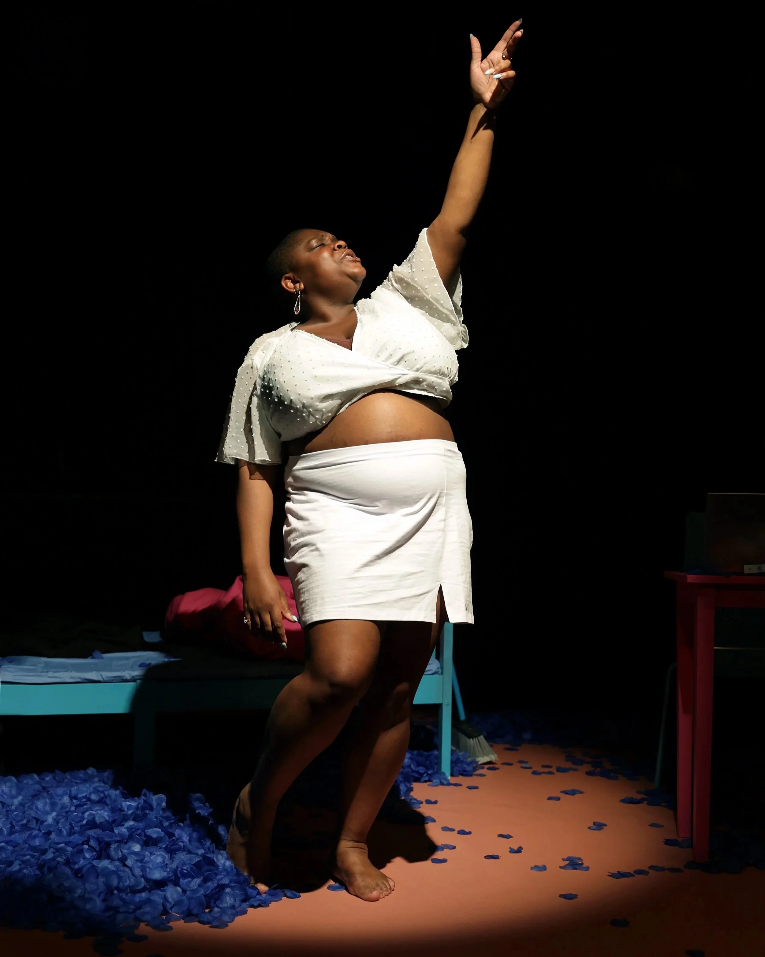 Maz - a fat Black nonbinary person - dressed in white, performing on stage