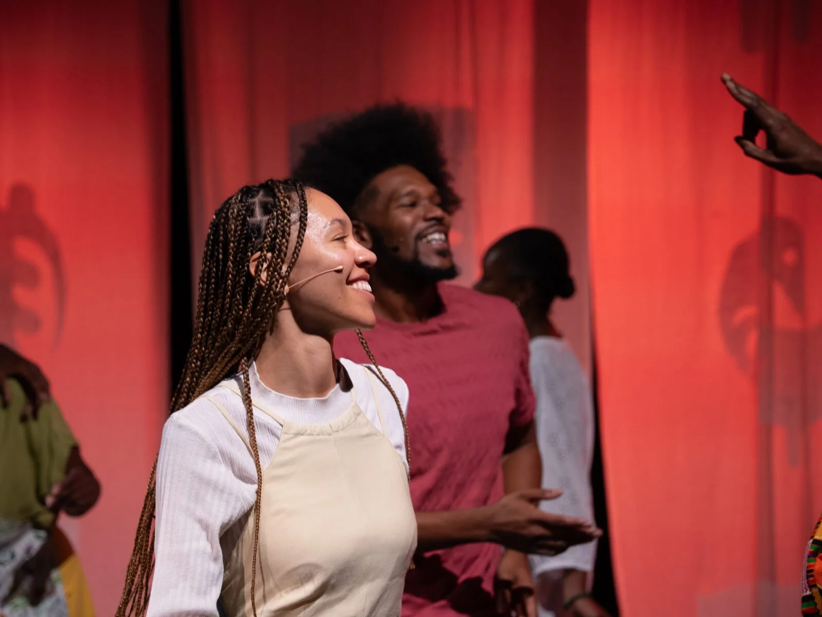 Four Black performers smiling and signing on stage with a red backdrop.