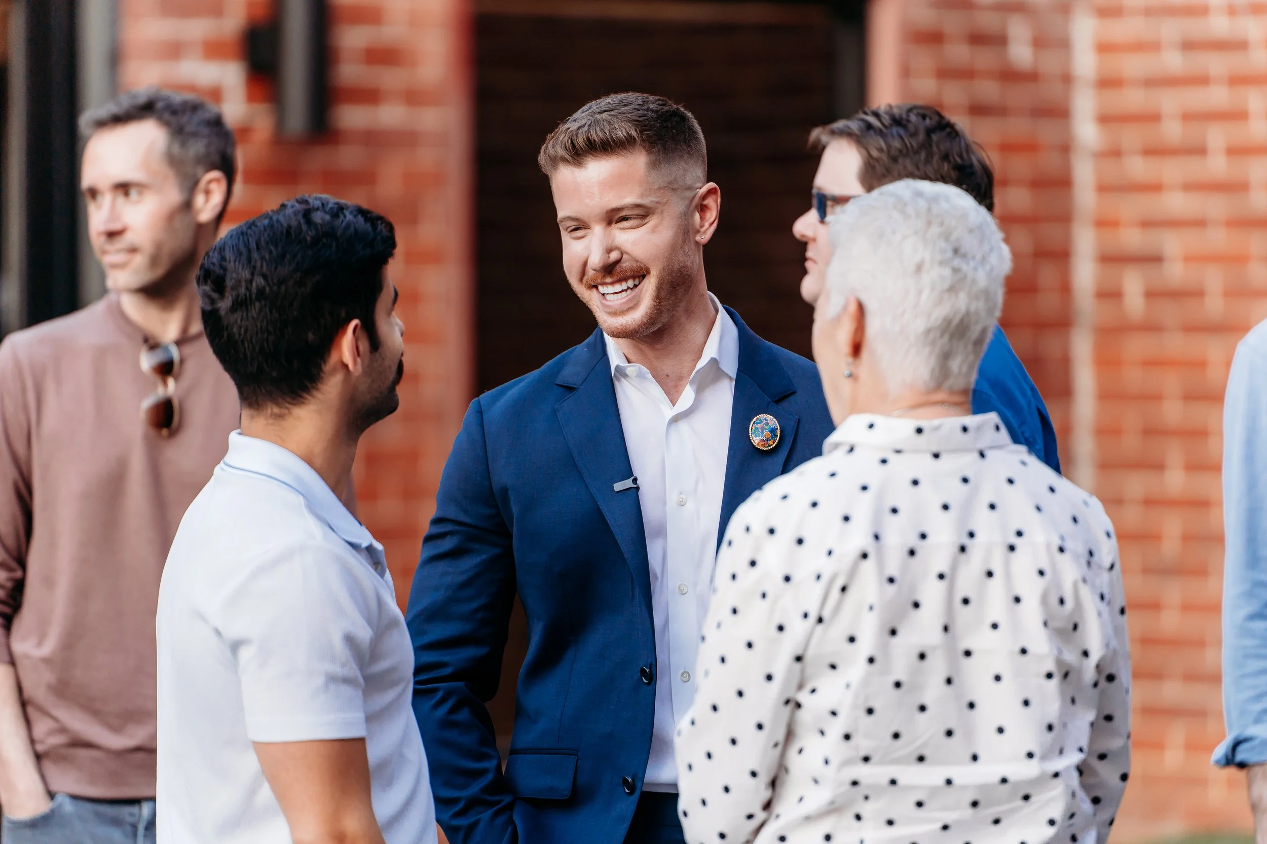 Blake Mitchell in a blue suit chatting with a group of people outside a brick building