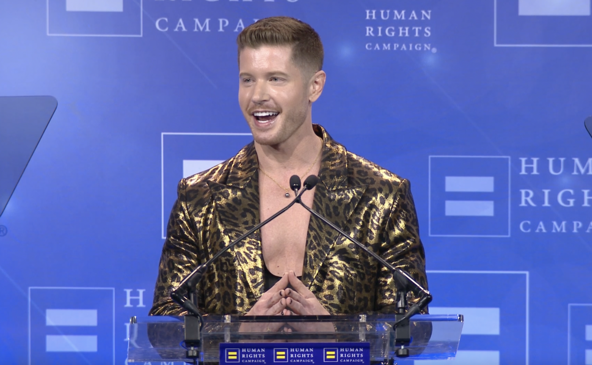 Blake Mitchell in a gold leopard-print jacket speaking at a podium for the Human Rights Campaign.