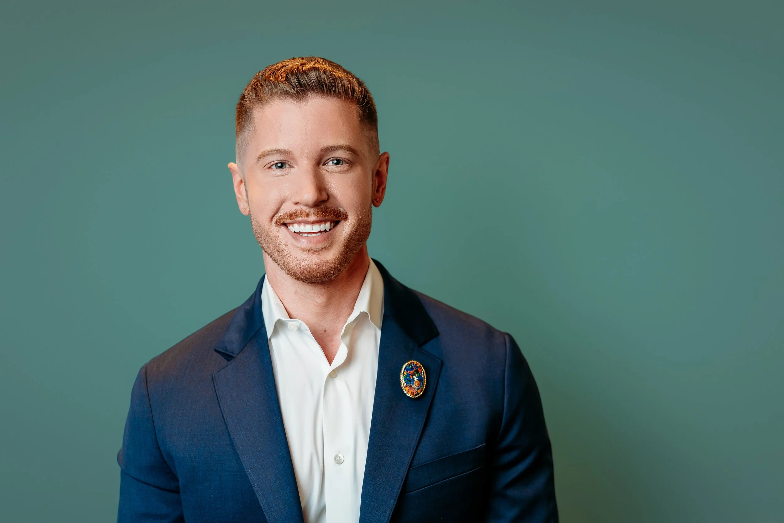 Blake Mitchell in a navy blazer and white shirt posing against a teal background