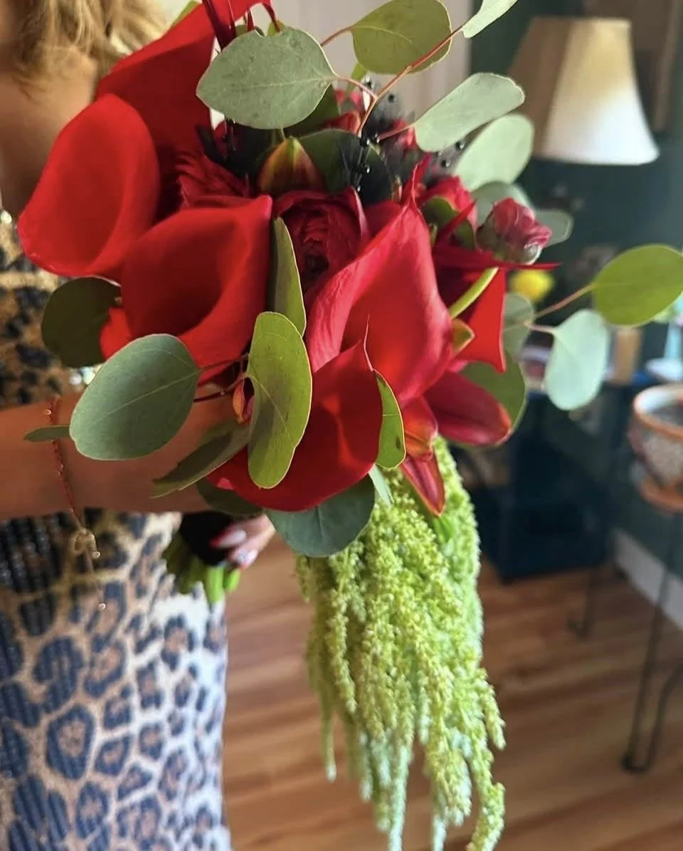 A bouquet of red flowers with green leaves in a green textured vase, held by a person wearing a leopard print dress.
