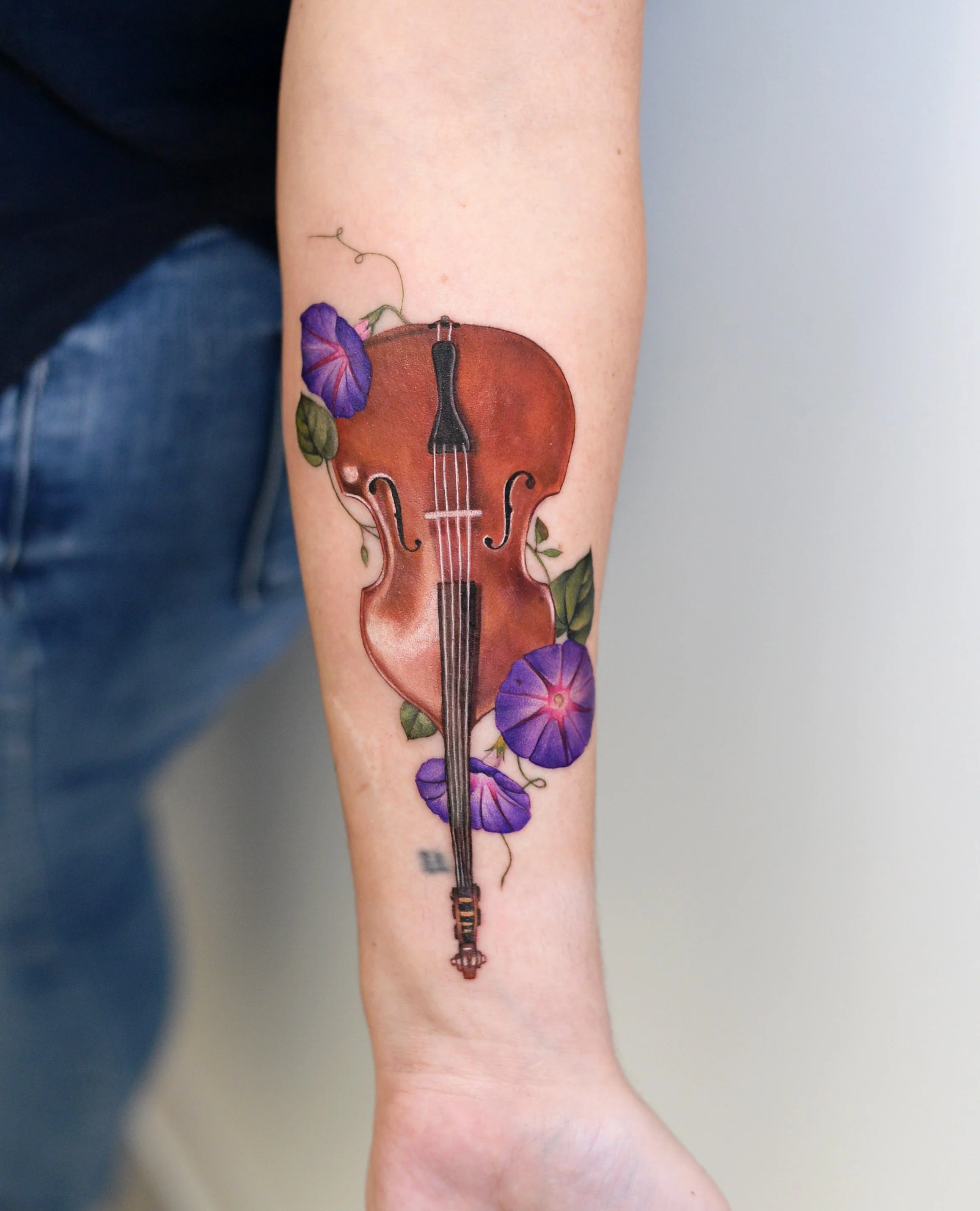 Tattoo of a detailed violin with purple morning glories on the person's forearm.