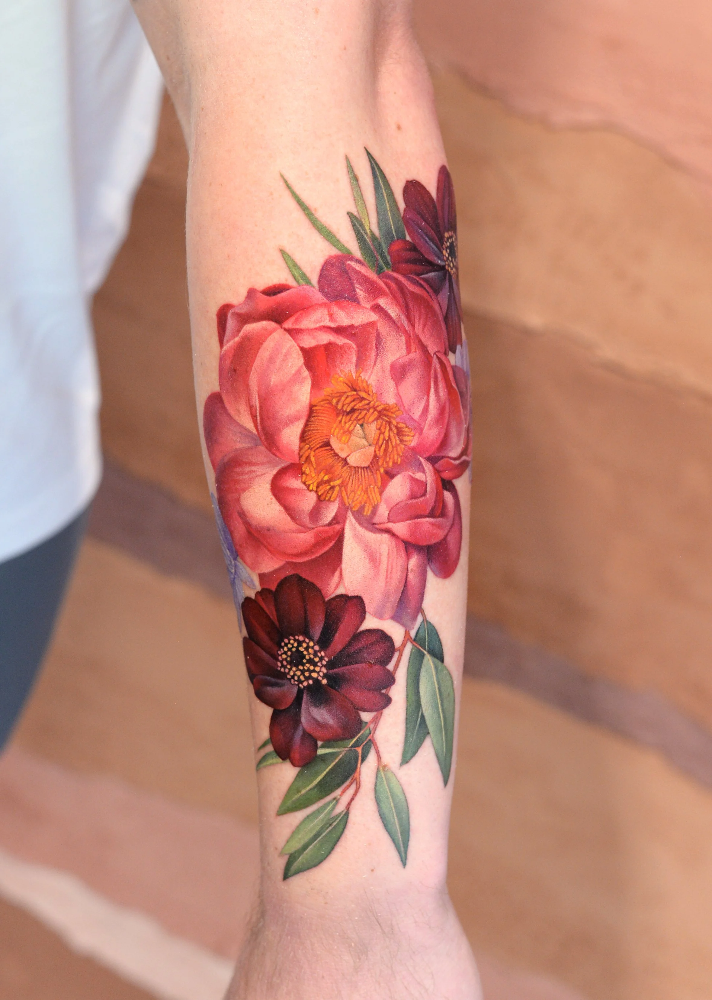A tattoo of various colorful flowers, including a red and pink rose with green leaves, on a person's arm.