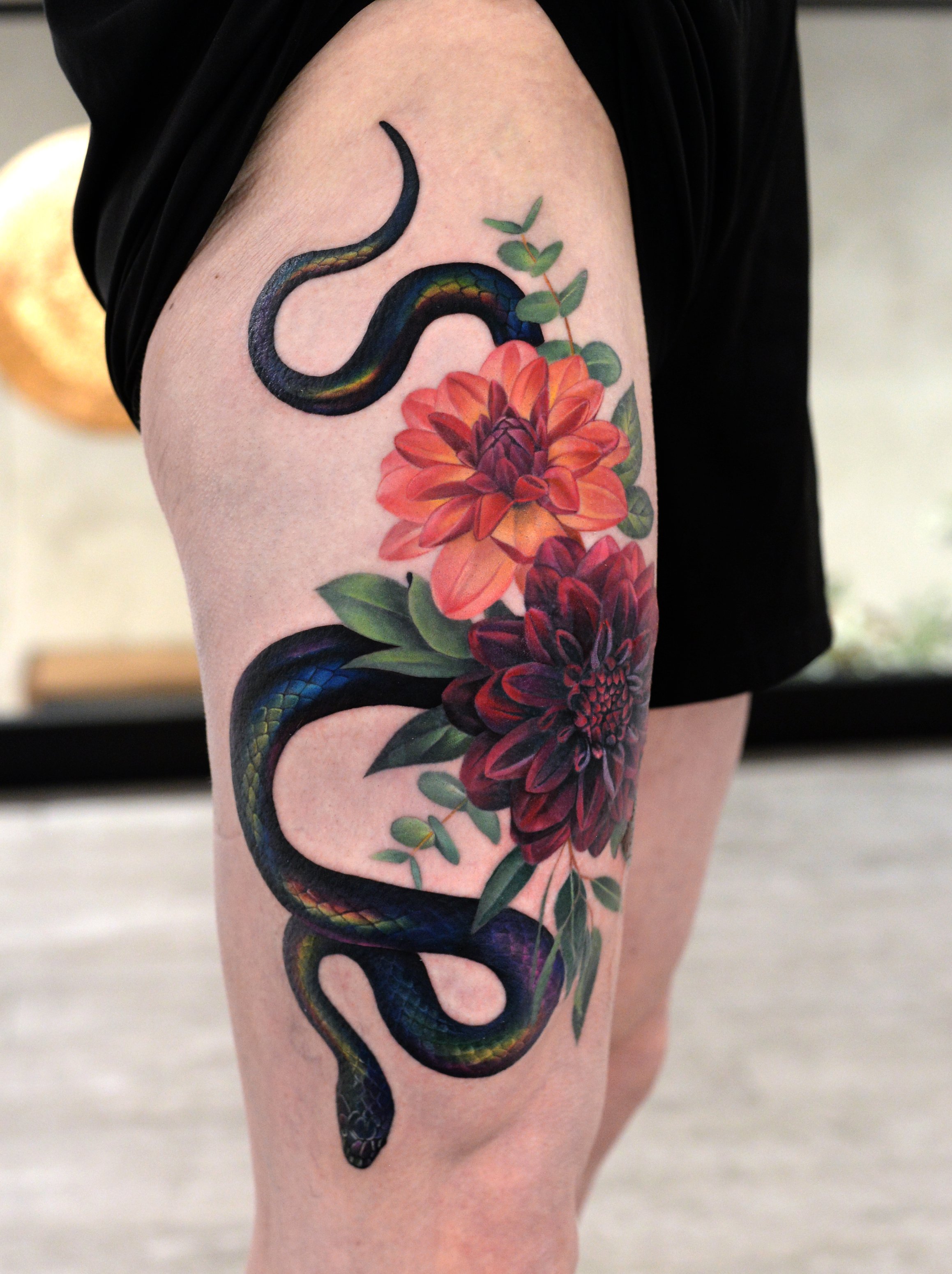 Tattoo of a dark-colored snake intertwined with vibrant red and purple flowers on a person's arm.