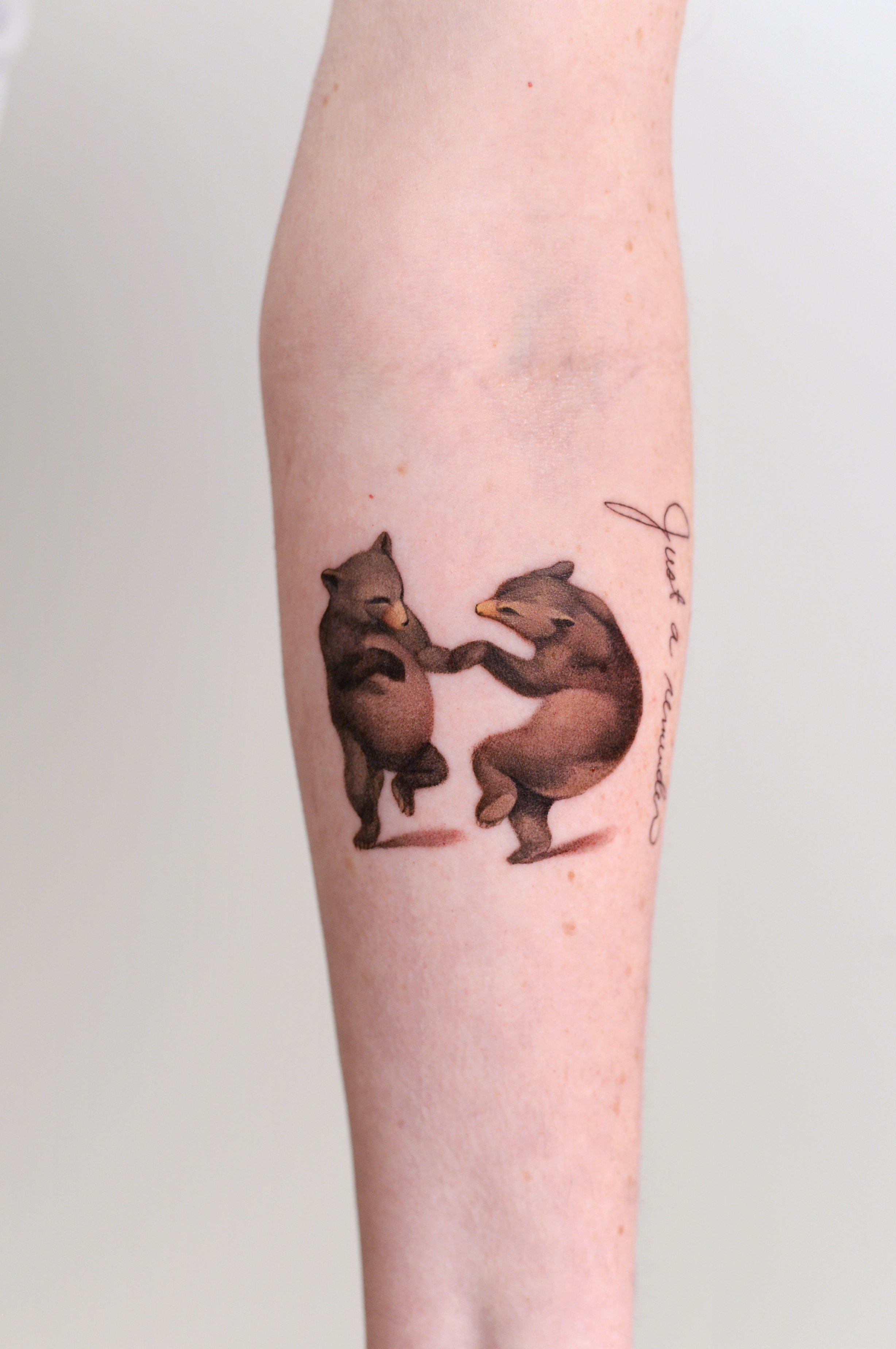 Tattoo of two wolves holding paws, with text in cursive on the side.