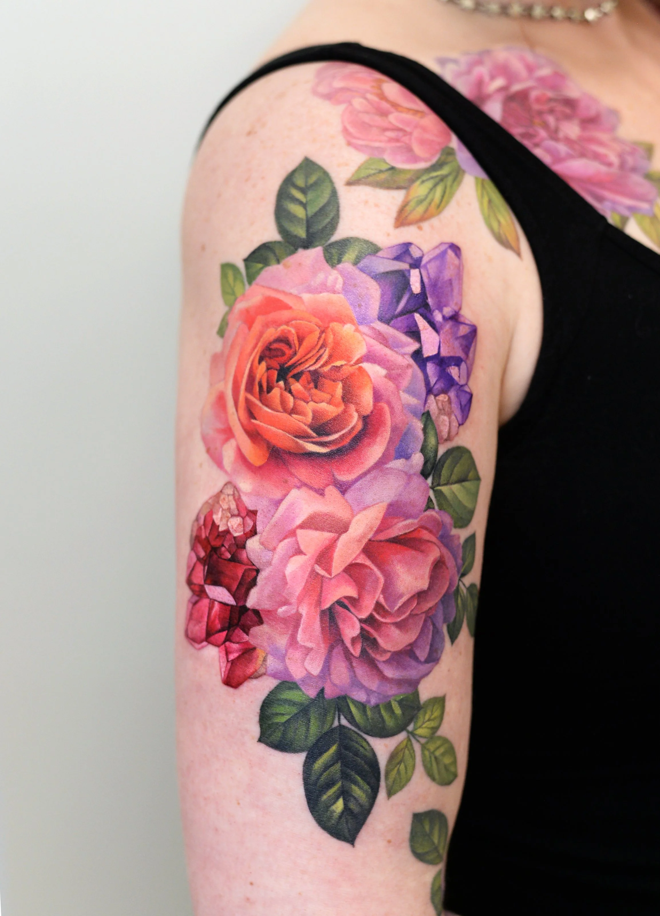 Close-up of a person's upper arm tattoo featuring colorful flowers, including roses and other blooms, with green leaves.