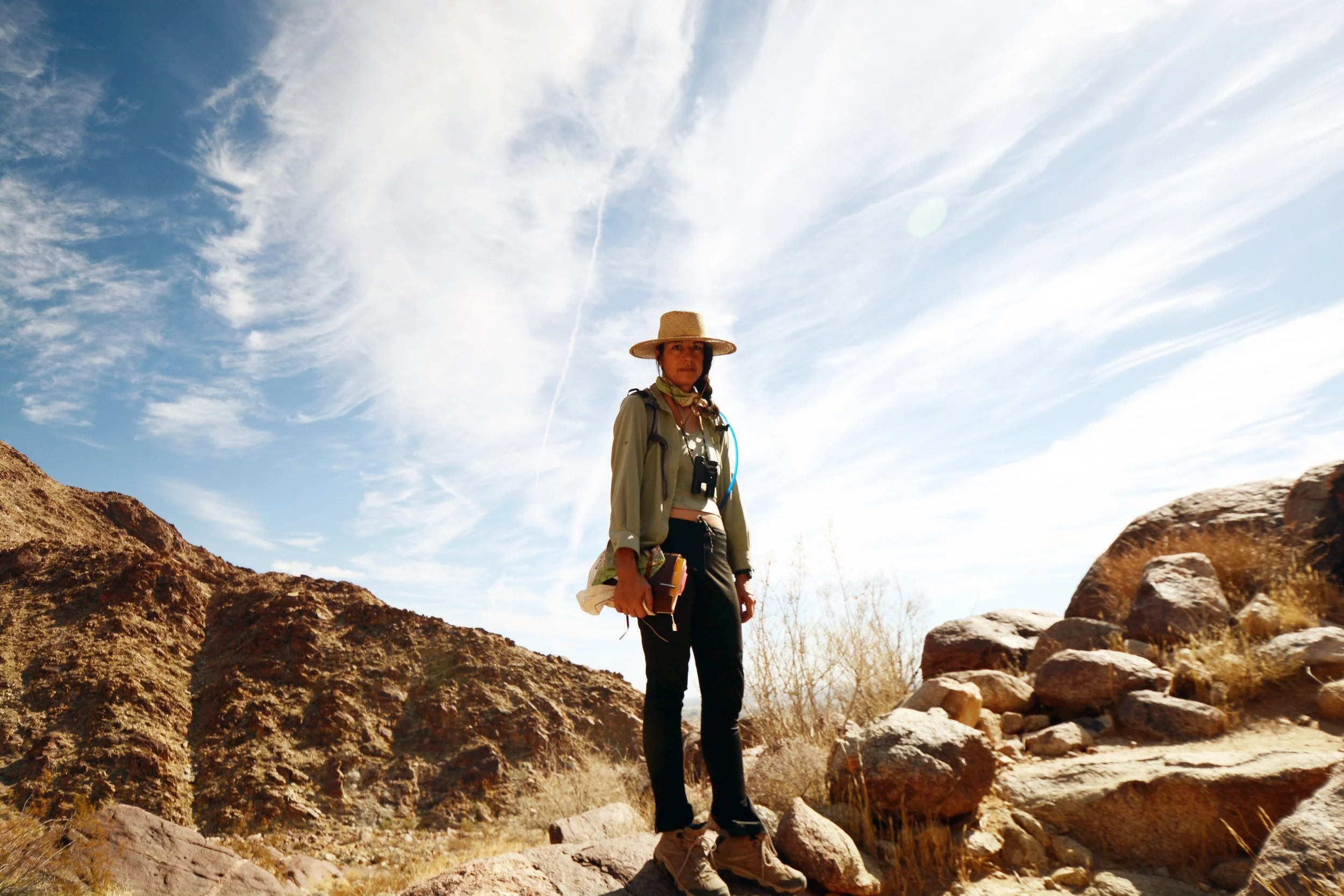 A woman hiking in a desert landscape with rocky terrain and a bright blue sky with some clouds.